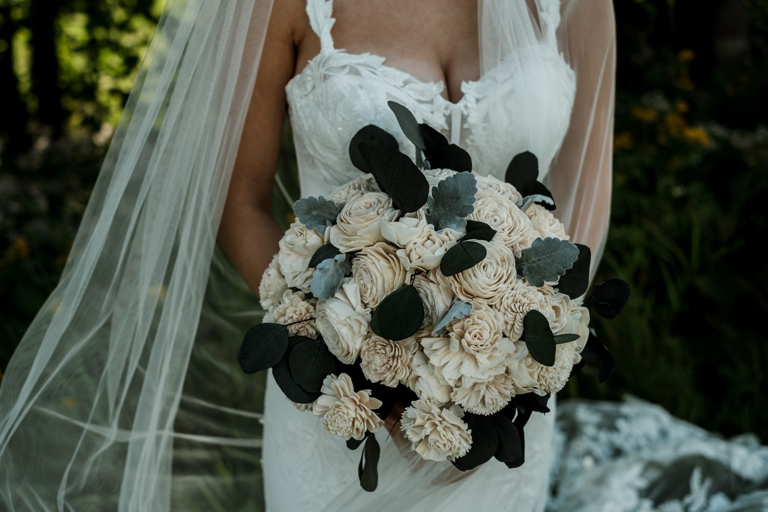 A bridal bouquet featuring white roses and dark foliage against a flowing veil.