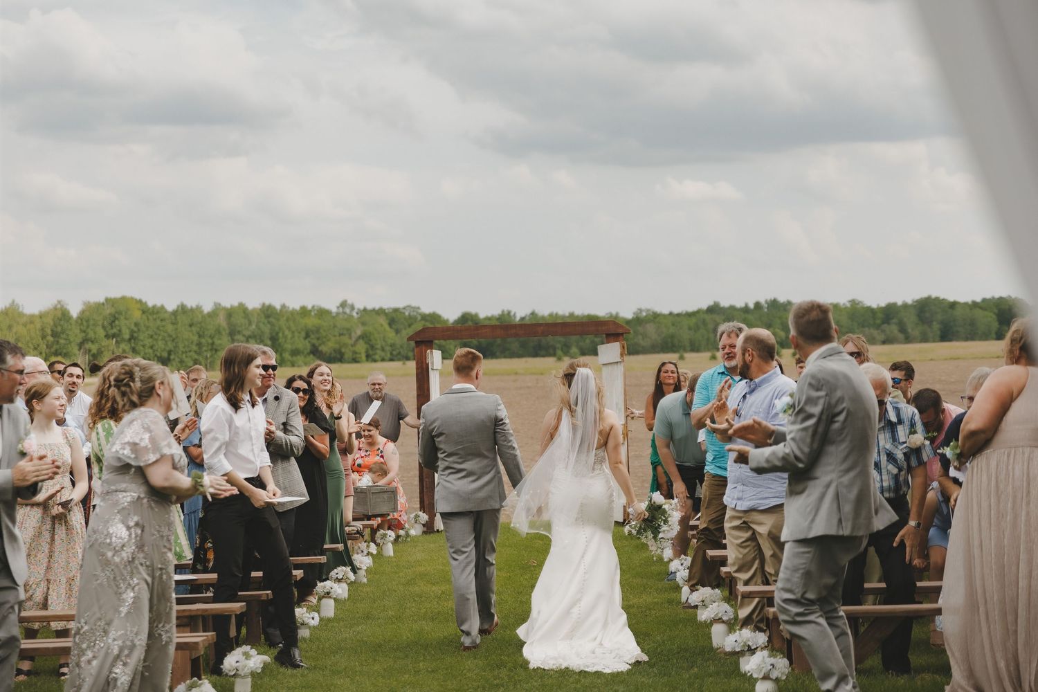 Bride and groom walk back down the aisle after their outdoor wedding ceremony as guests celebrate.