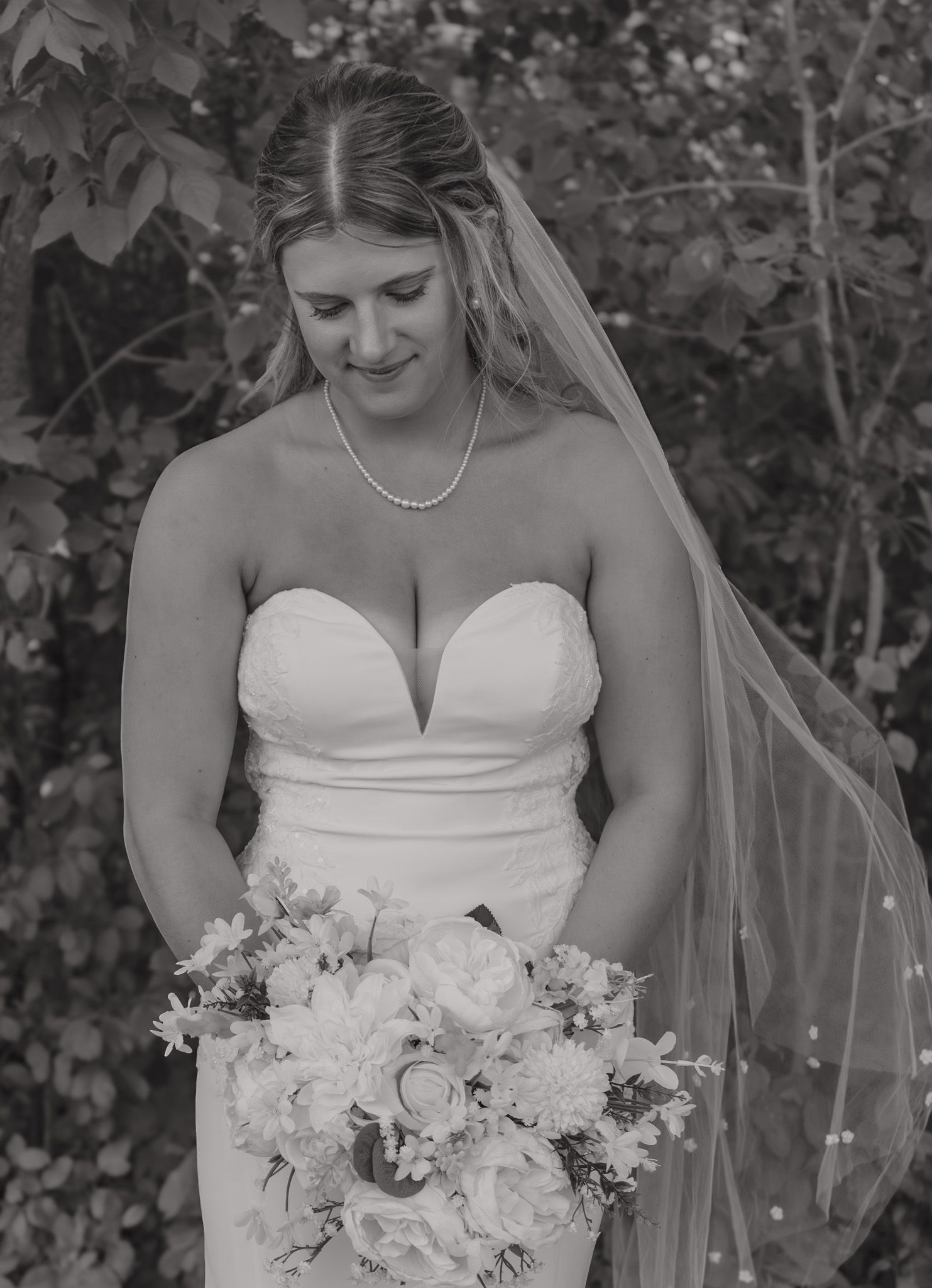 Black and white portrait of smiling bride in strapless gown holding floral bouquet with veil.