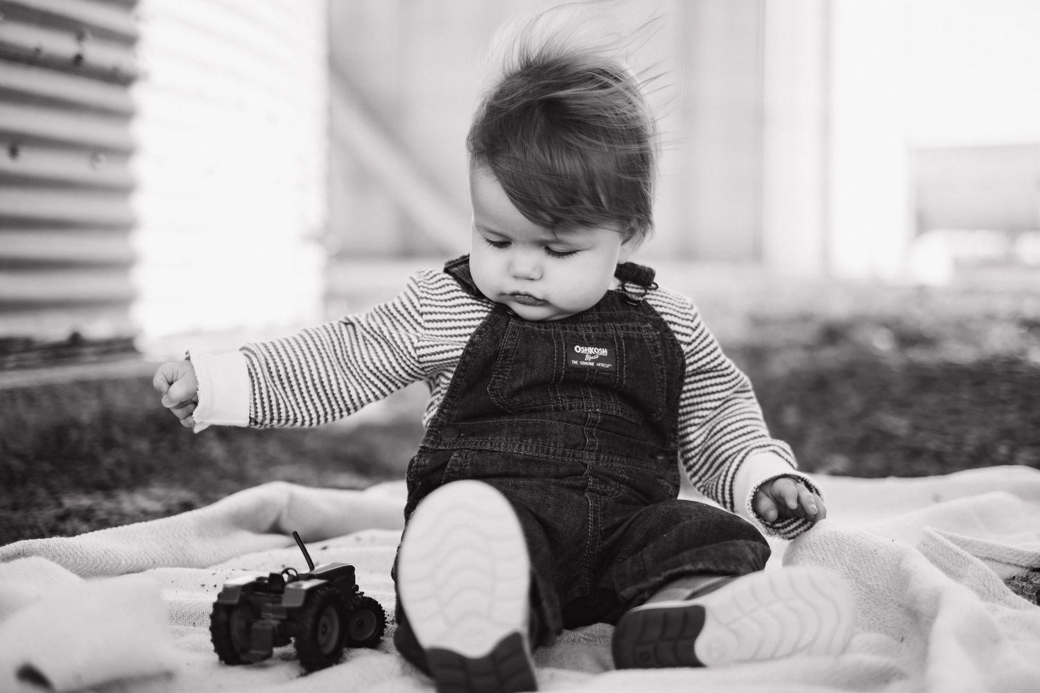 Small child in overalls and striped shirt playing on white bedding.