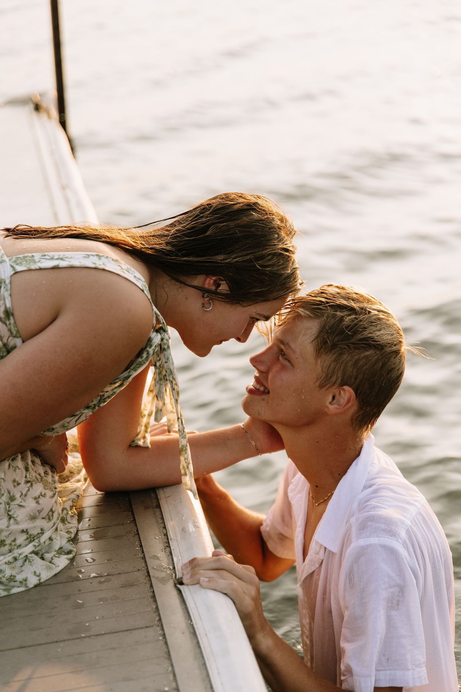 Romantic couple sharing a tender moment on a wooden dock by the water at golden hour sunset.