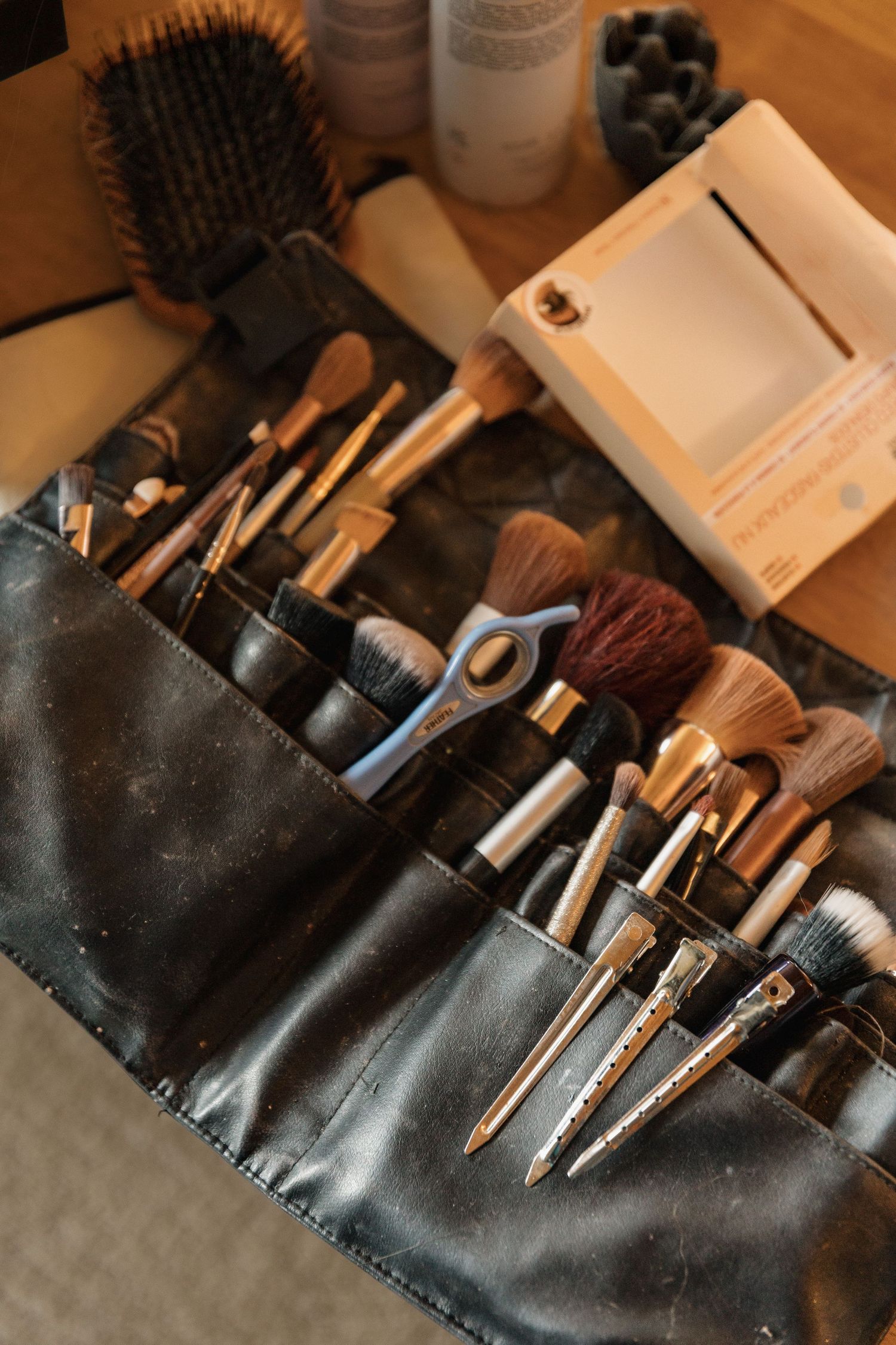 Professional makeup artist brush set organized in a leather roll case on a wooden vanity table.