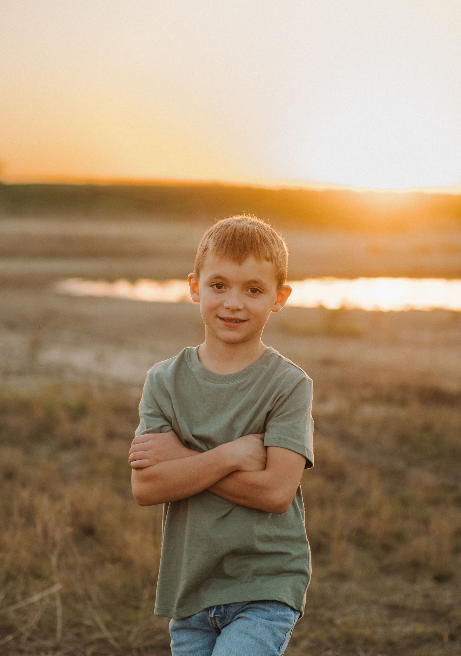 Child in green t-shirt and jeans smiling during golden hour sunset.