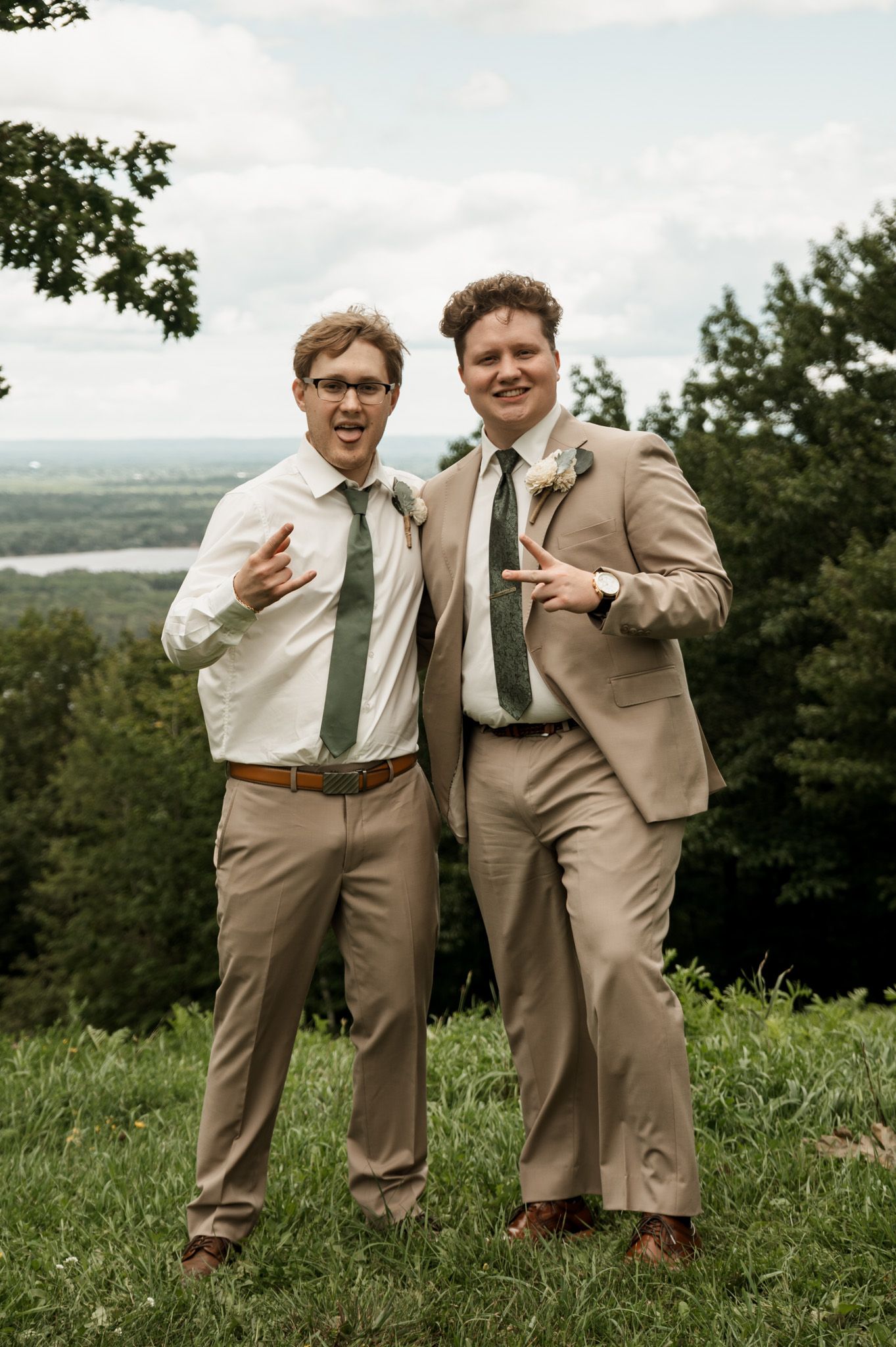 Wedding party in khaki suits shares laughs and candid moments on a grassy overlook.