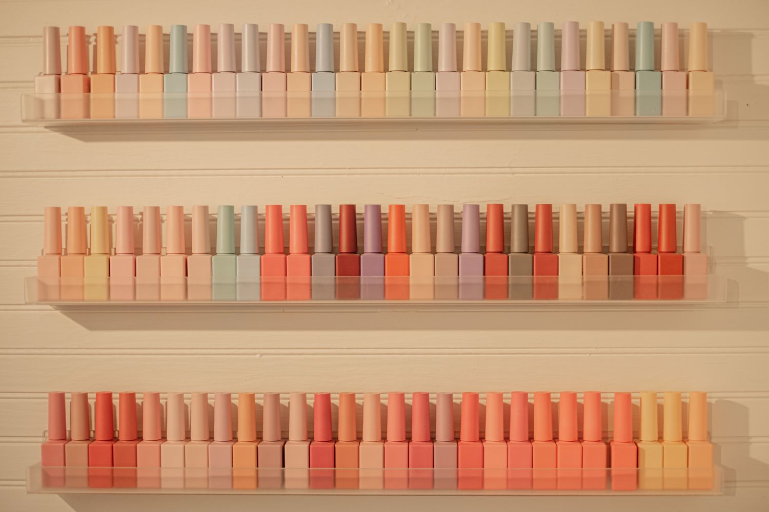 Colorful nail polish bottles arranged in rows on white floating shelves.