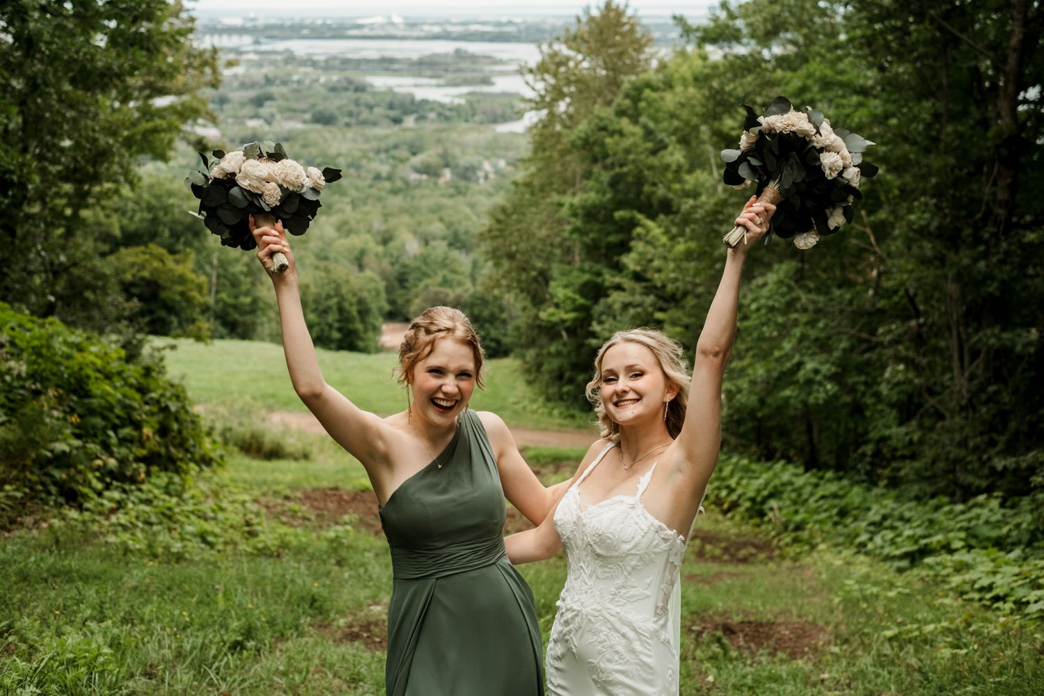 Wedding party celebrates with arms raised against scenic natural backdrop.