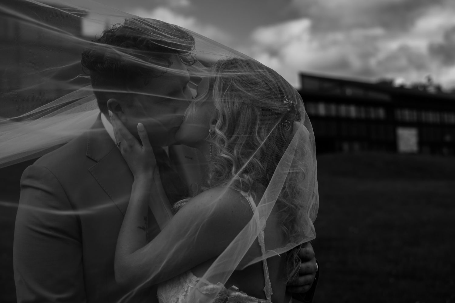 Silhouetted wedding couple embraces against a dramatic sky in black and white.