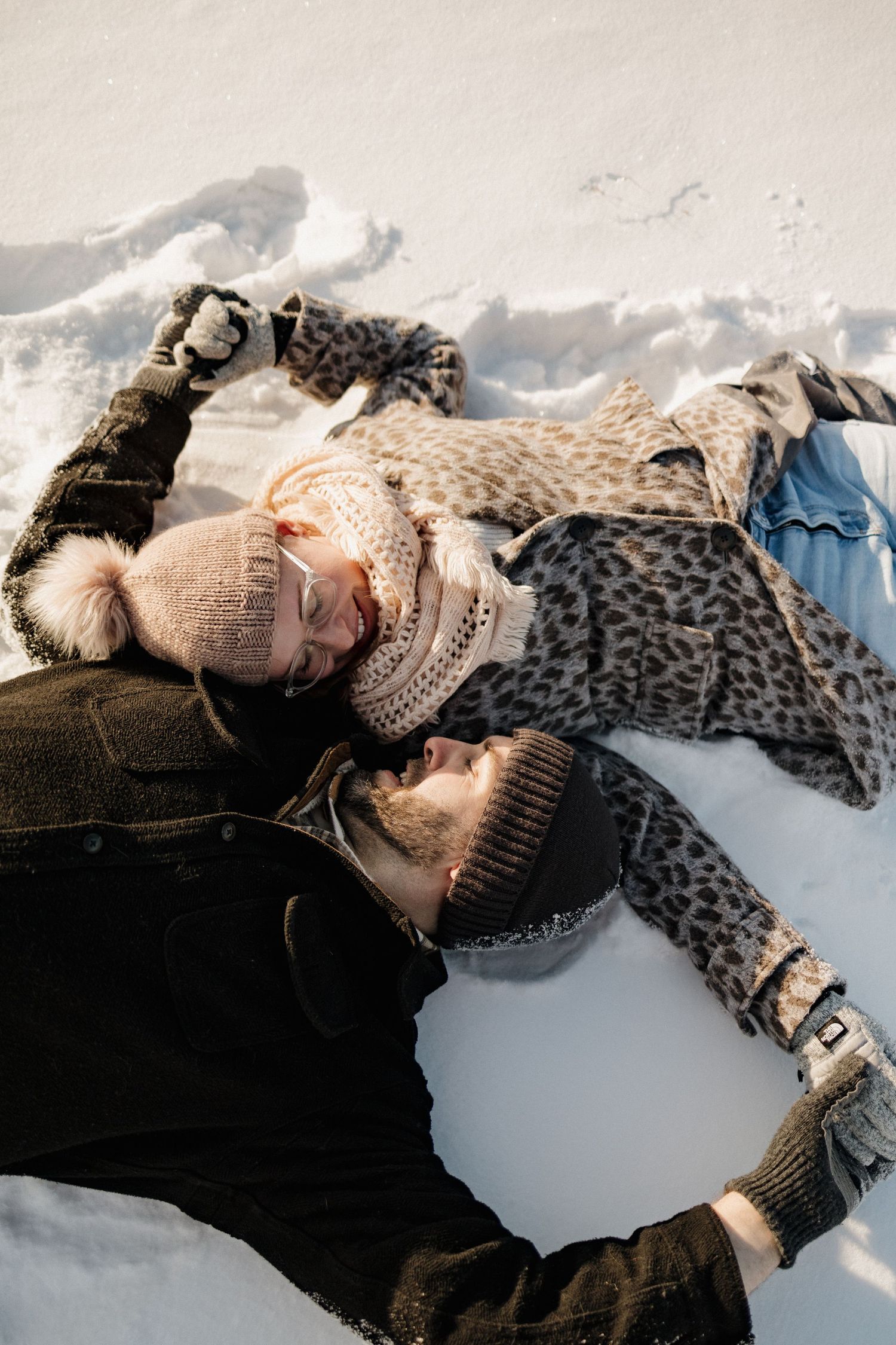 A person lying in the snow wearing a knit hat and leopard print coat rests against a dark winter background.