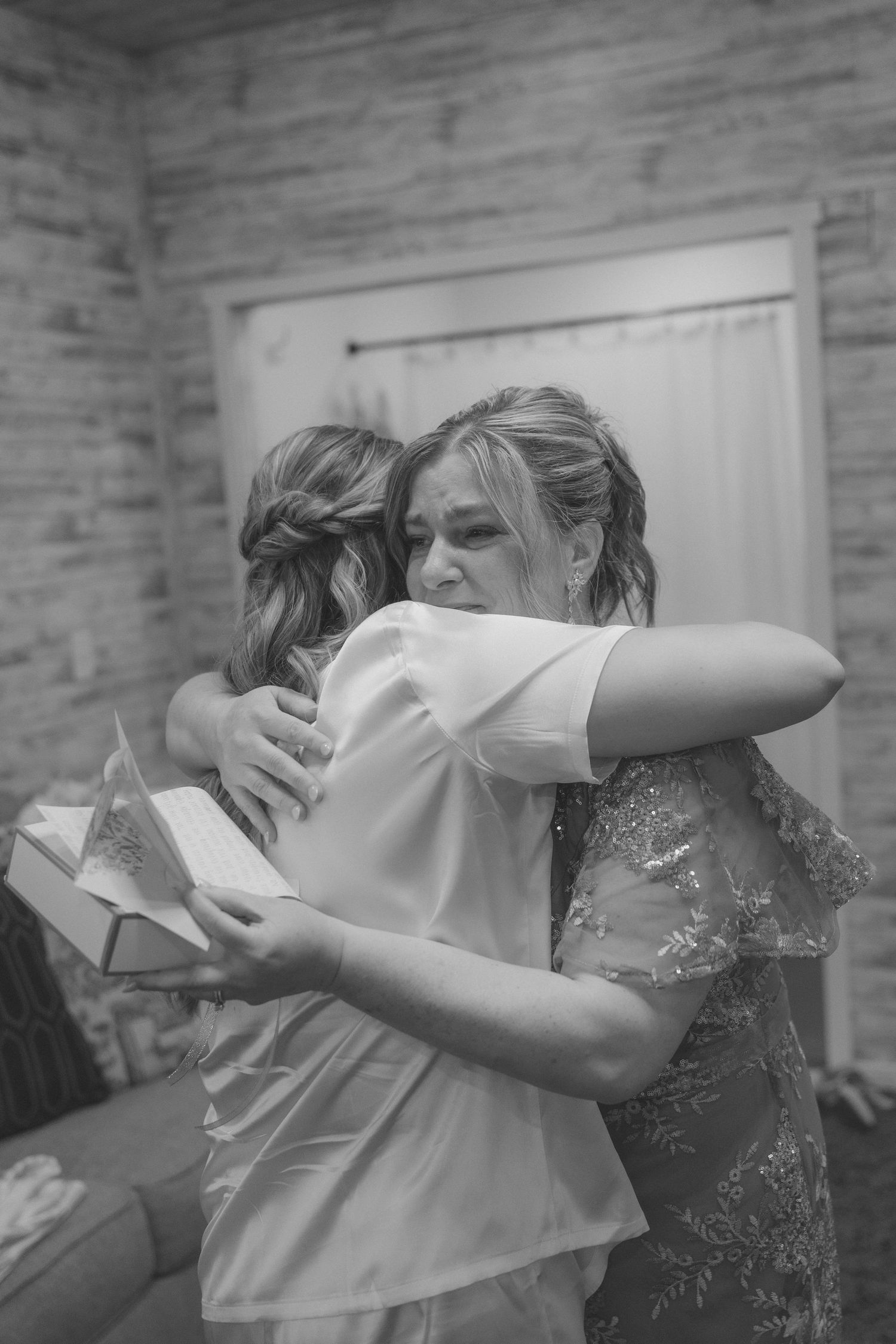 Black and white photo of two women in formal attire sharing an emotional hug at a wedding celebration.