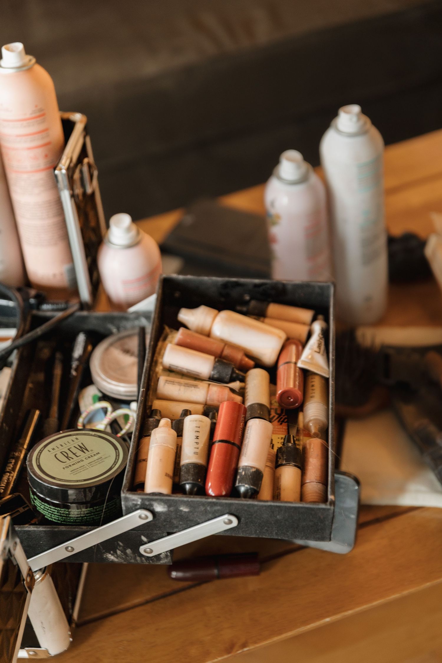A makeup artist's metal toolbox filled with lipsticks, foundations, and beauty products on a wooden table.