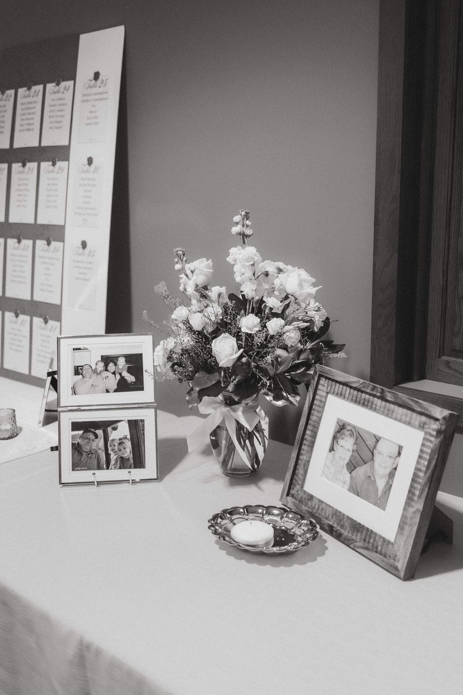 Black and white wedding reception table with framed photos, roses, and seating chart display.