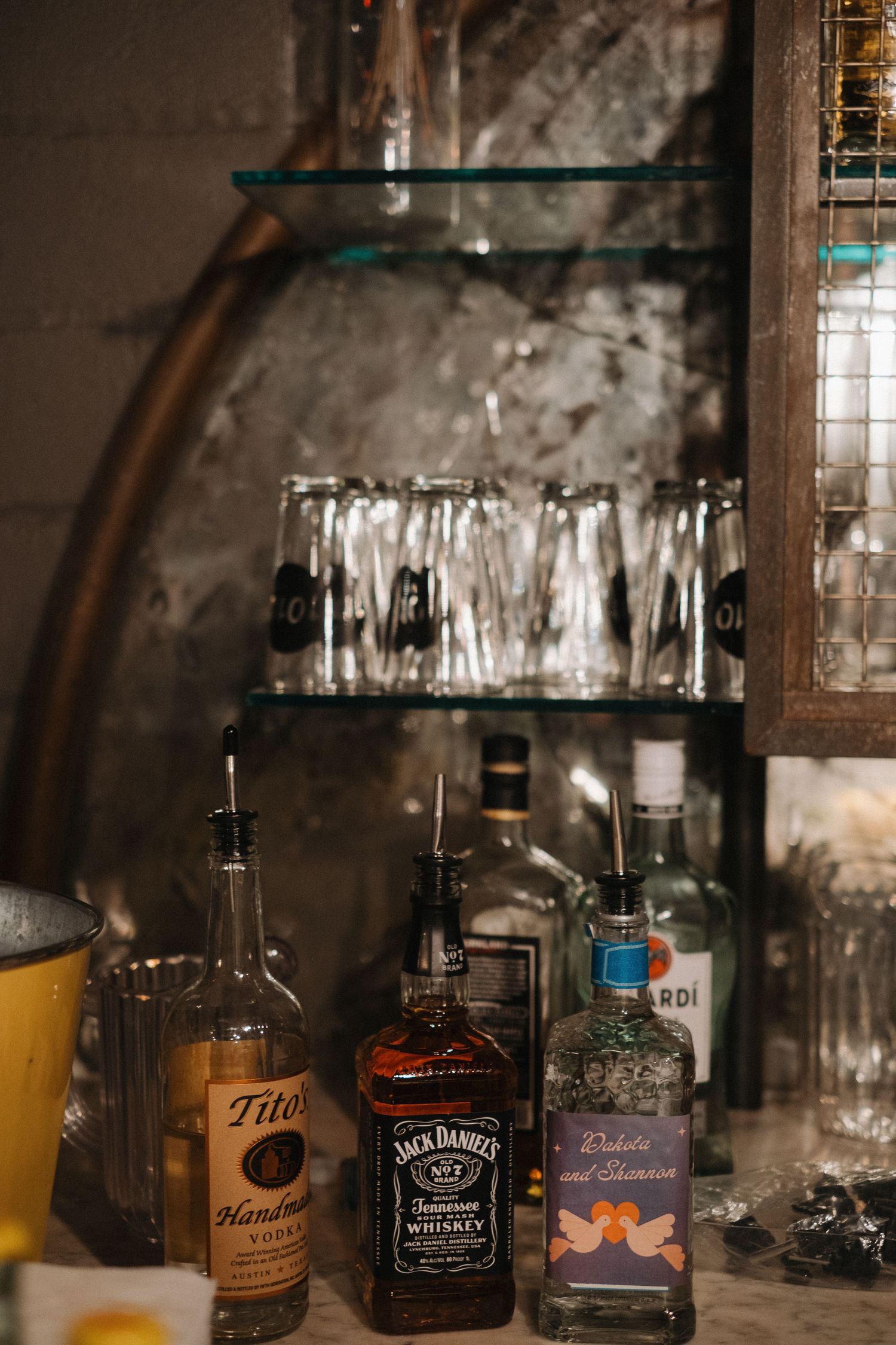 Bar setup with various liquor bottles including Jack Daniels and Tito's displayed on rustic shelving.