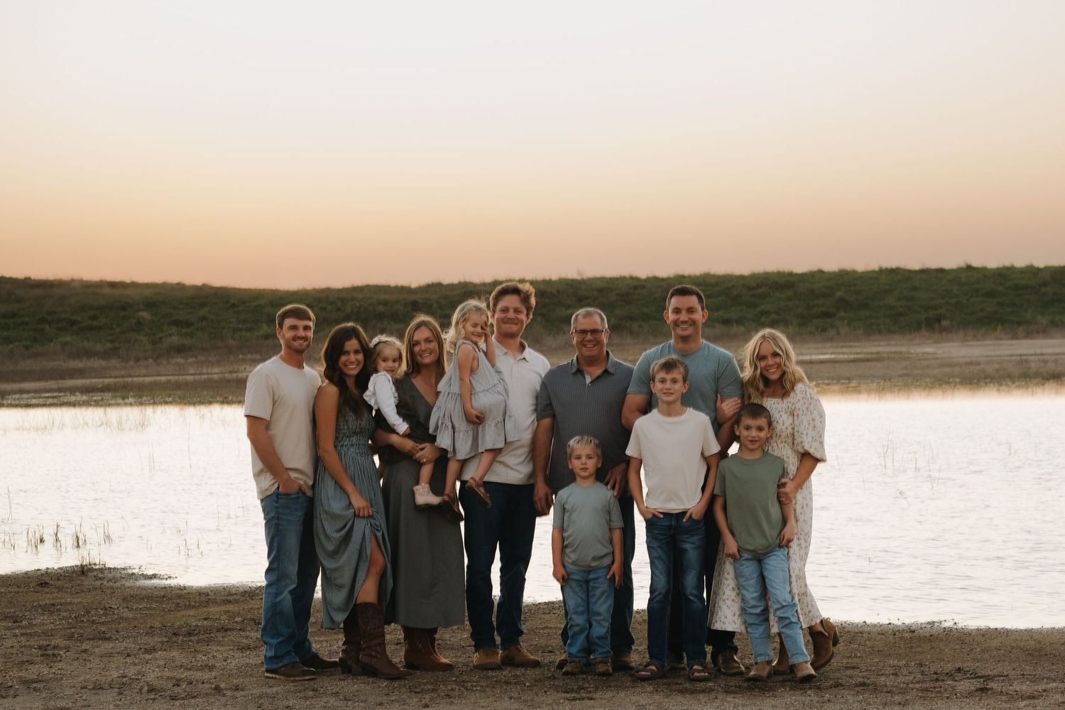 Large family group wearing coordinated blue and neutral tones poses together at sunset.