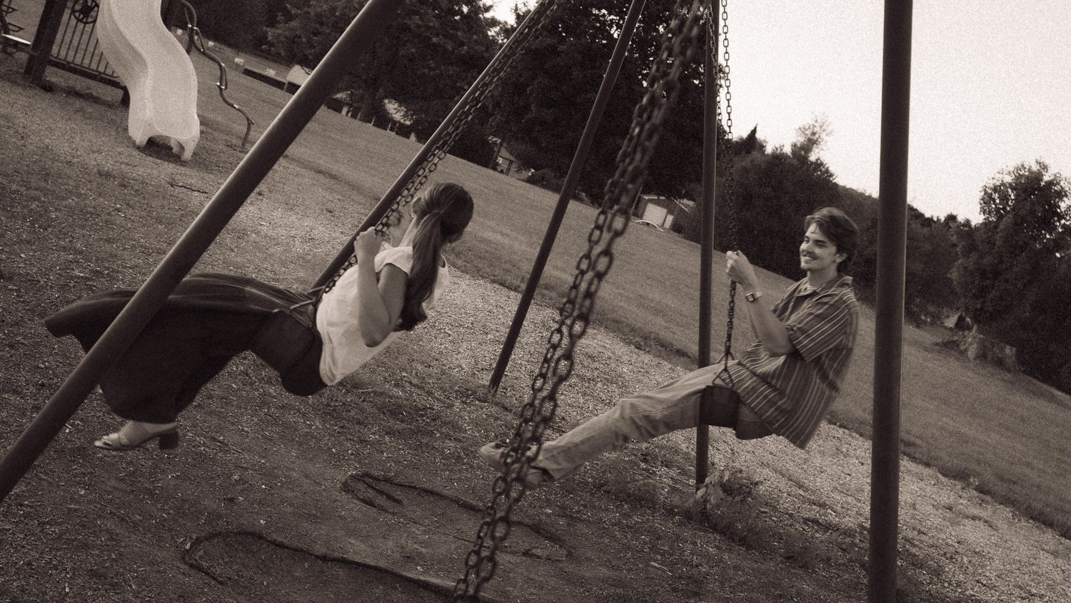Two children playing on swings in a park, captured in a nostalgic black and white photograph.