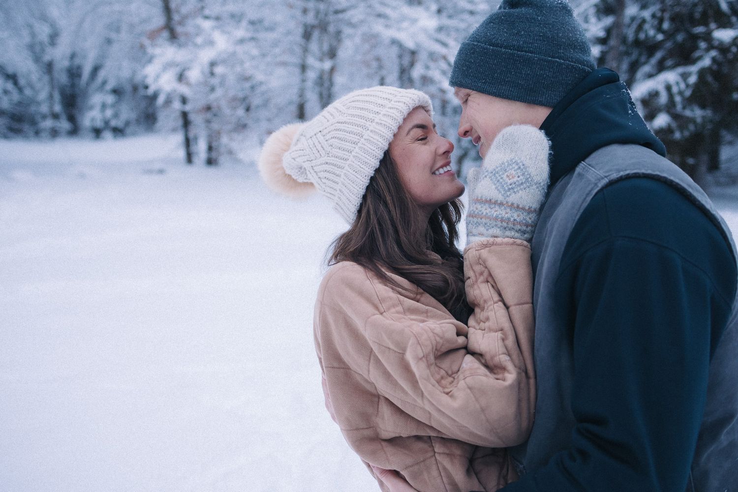 Couple sharing a romantic moment in a snowy winter wonderland, wearing cozy hats and mittens.