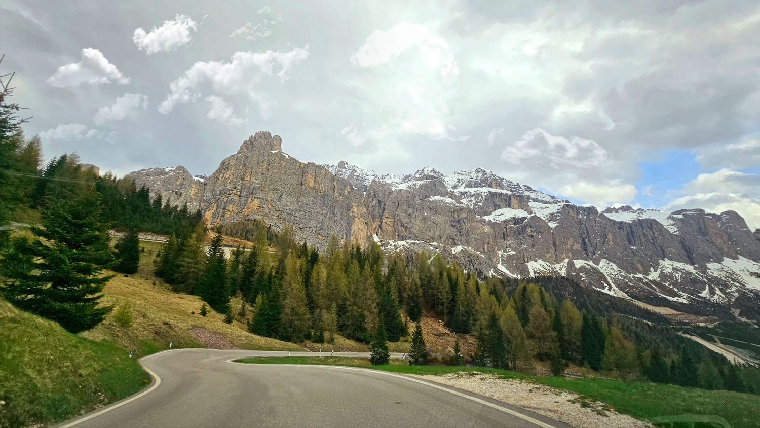 Scenic mountain road winding through Dolomites with dramatic rocky peaks and green valley.