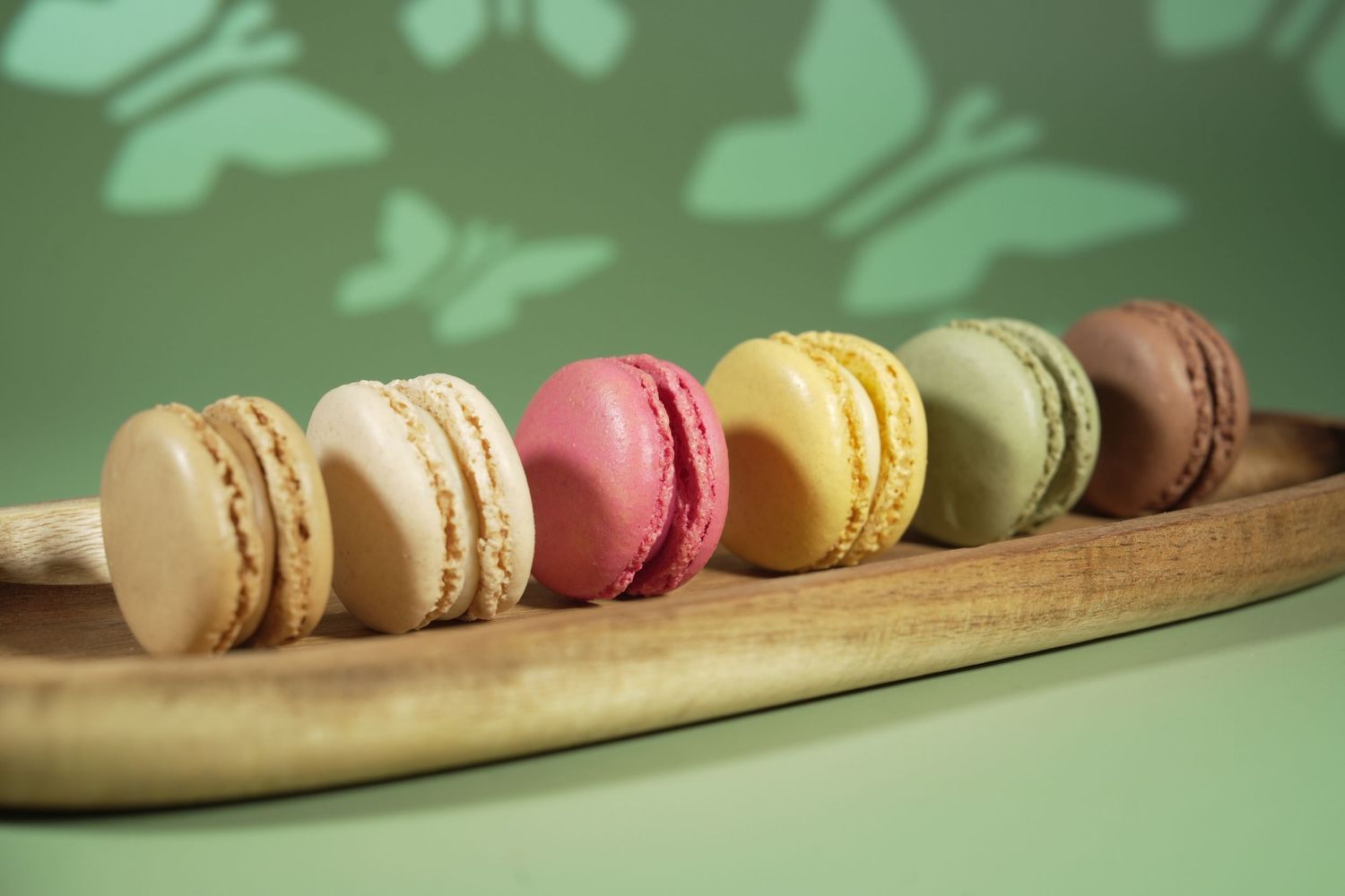 Colorful French macarons in various flavors arranged in a line on a wooden serving board.
