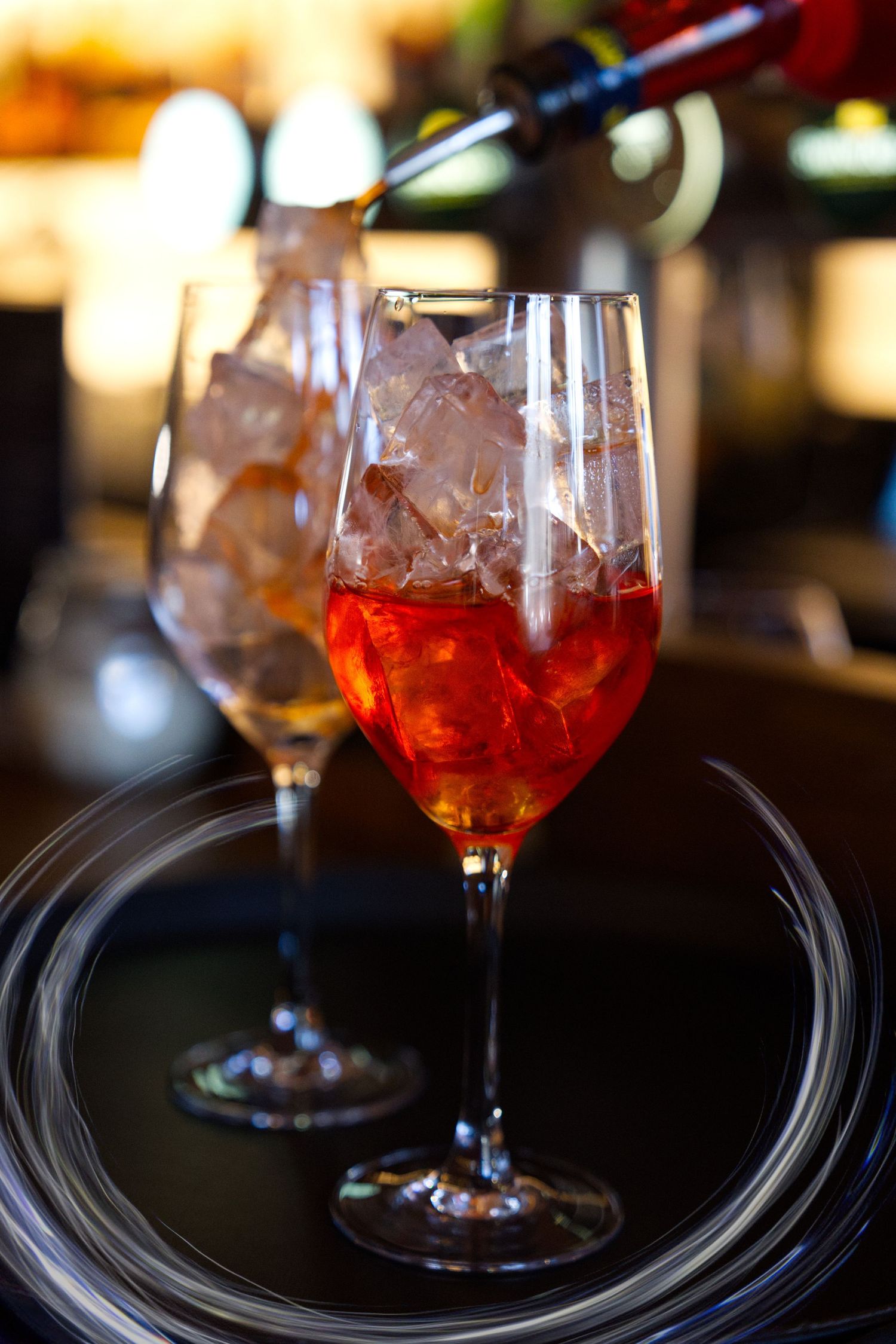 Four glasses of Aperol Spritz cocktails lined up on a dark bar counter with blurred background lighting.