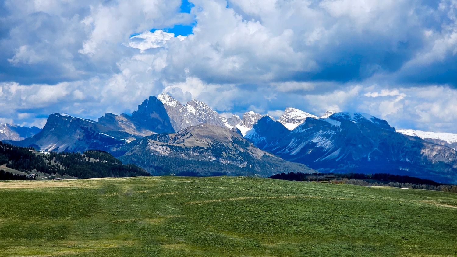 Panoramic mountain landscape with snow-capped peaks and blue sky with white clouds.