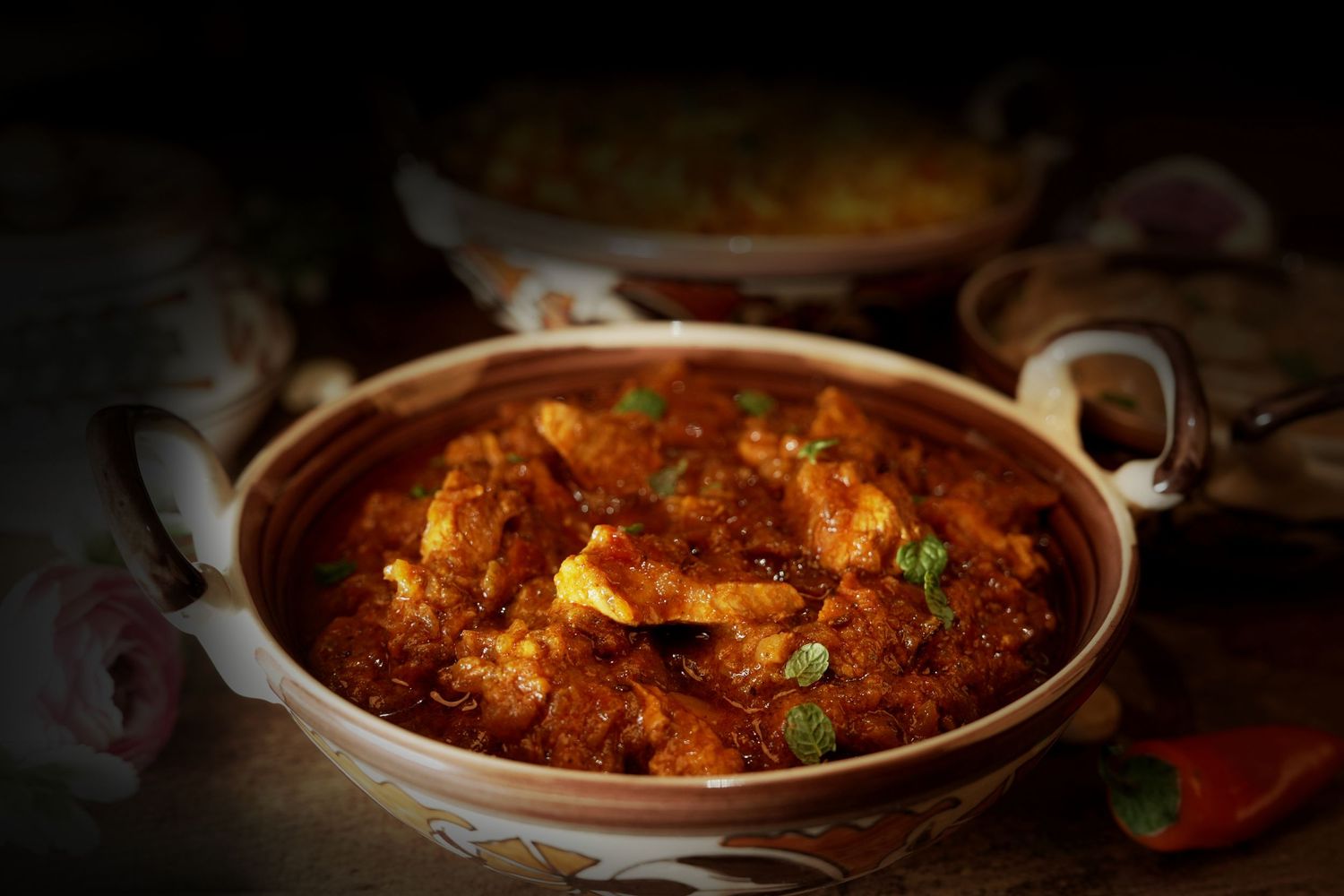 Spicy curry served in an earthenware bowl with vibrant red sauce and fresh herbs.
