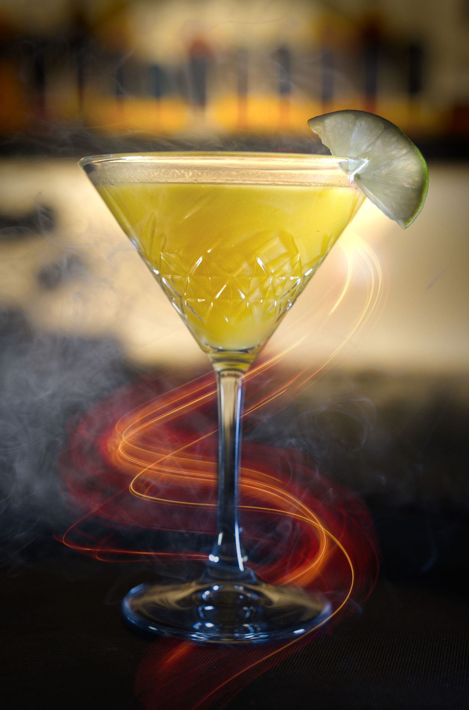 A martini glass filled with yellow cocktail creates light trails and smoke effects in a dramatic photo sequence.