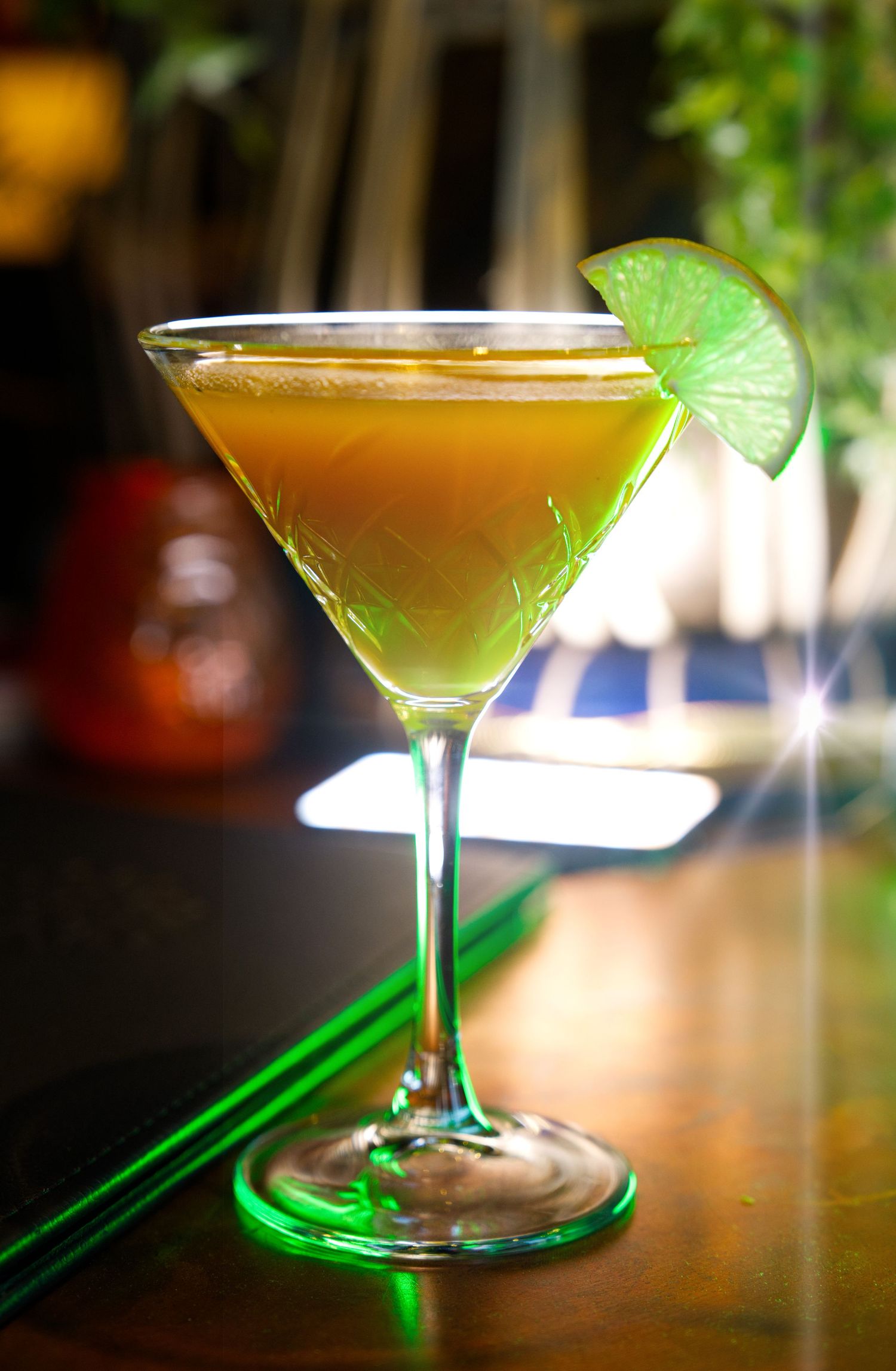 A golden martini cocktail garnished with a fresh lime wedge served in an elegant stemmed glass on a wooden surface.