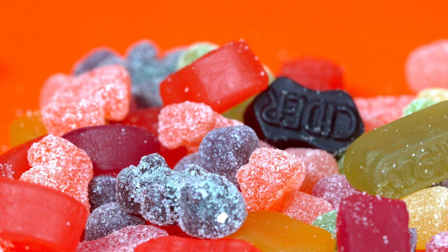 Colorful assorted gummy candies and jellies on bright orange background.