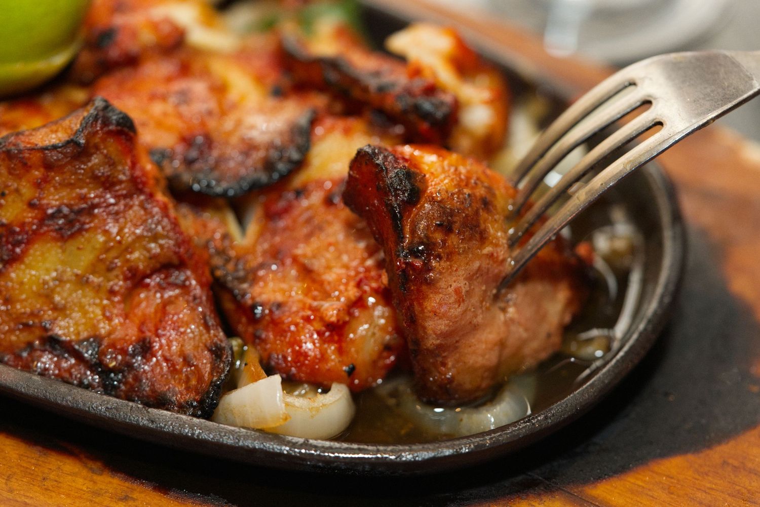 Grilled teriyaki chicken pieces with caramelized glaze on a sizzling cast iron plate.