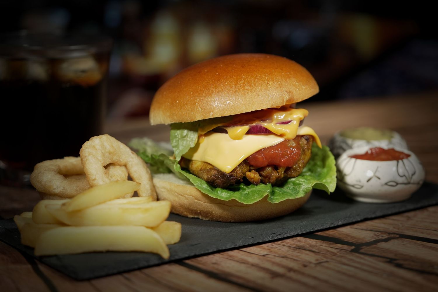 Gourmet burgers with fresh lettuce and onion rings served on black slate plates.