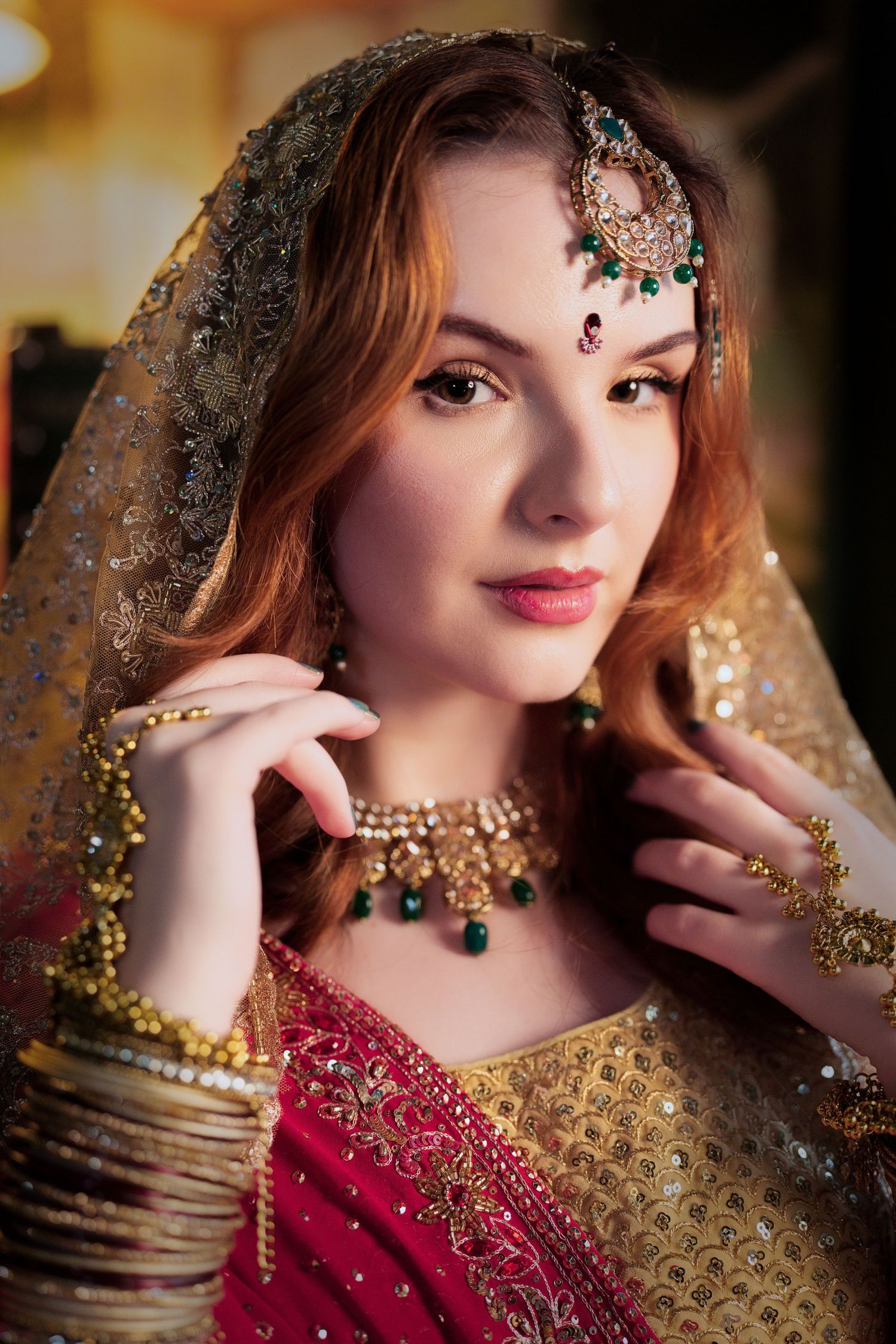 South Asian bridal portrait with emerald jewelry and gold embroidered red dress.