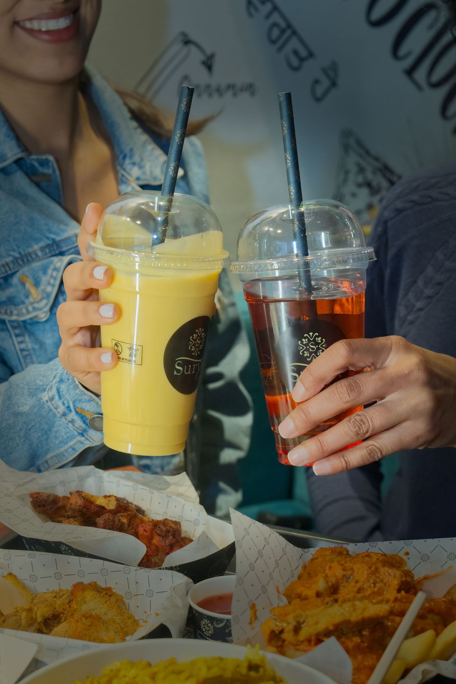 Hands holding colorful beverages and sharing crispy fried chicken tenders with french fries at a casual dining restaurant.