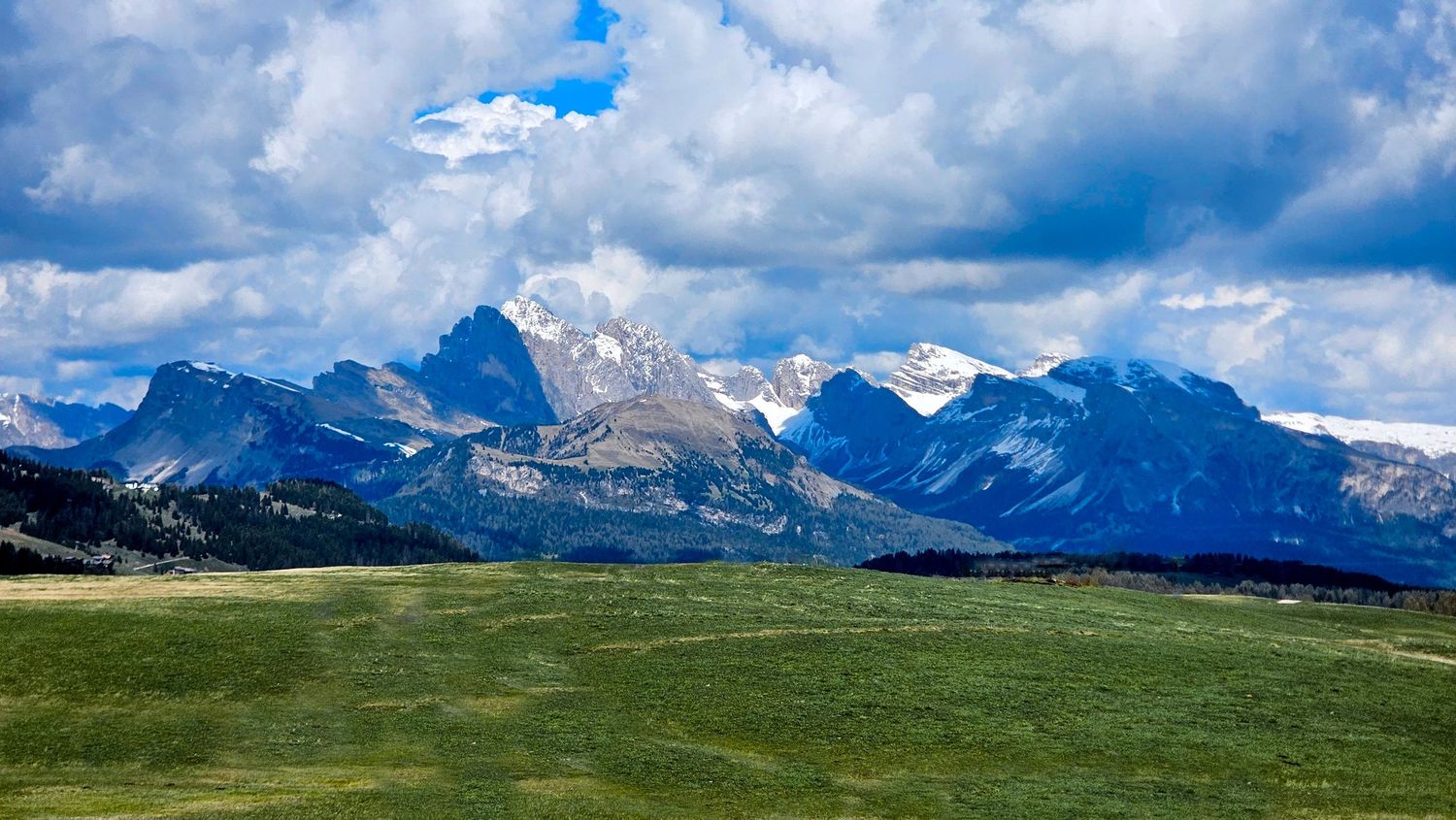 Dramatic mountain landscape with snow-capped peaks under blue sky with puffy clouds.