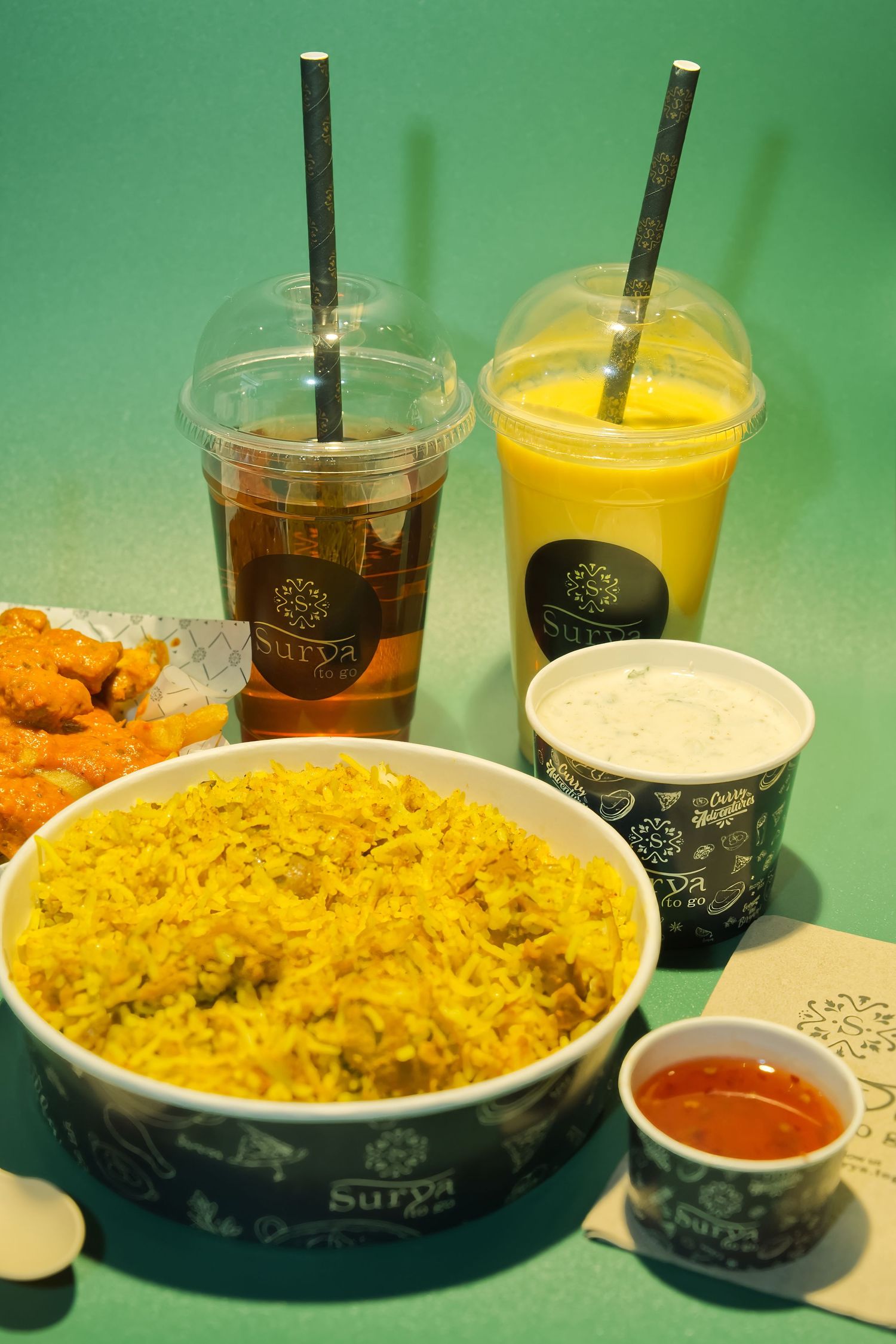 A series of fast food items including rice, drinks, and sauces arranged on a green background with black cups and bowls.