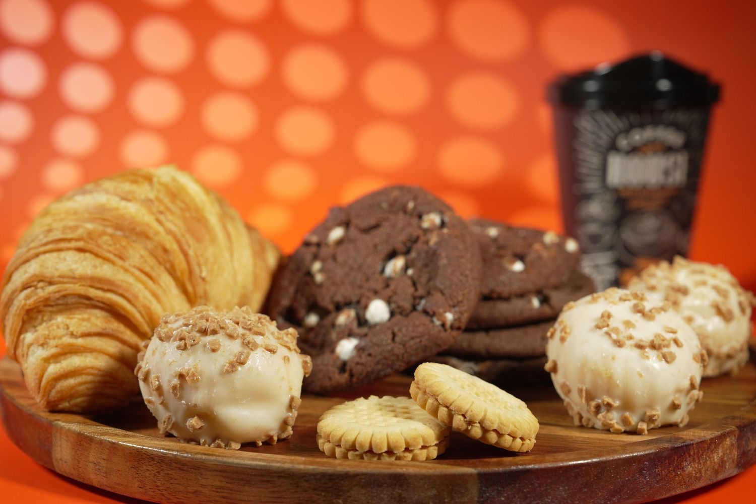 Assorted pastries including croissant, cookies and decorated donuts on wooden board.