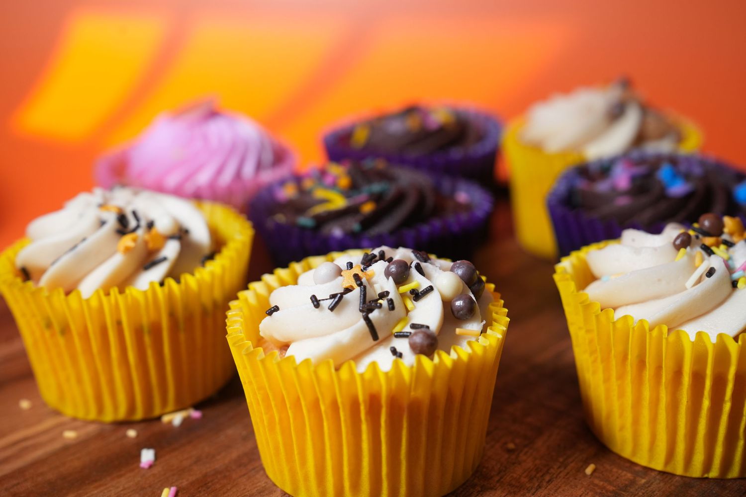 Yellow cupcakes topped with colorful frosting and chocolate sprinkles on a wooden surface.