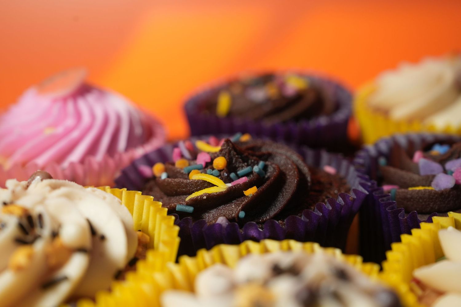 Assorted chocolate cupcakes with frosting in yellow paper liners.