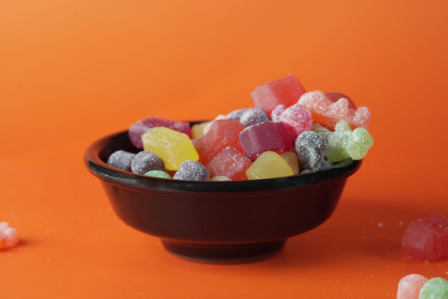 Colorful gummy candies and sweets arranged on dark plates against orange background.