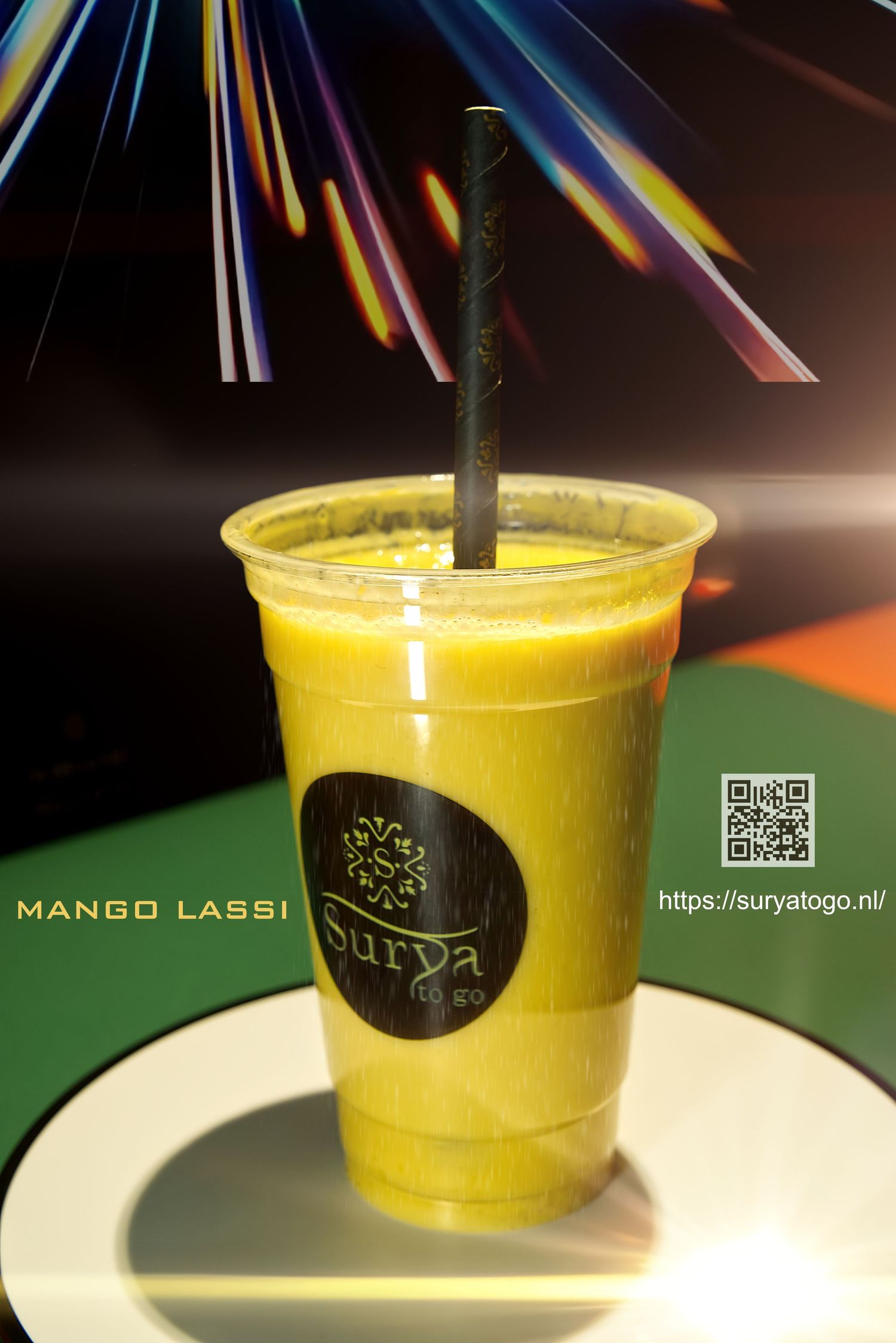 A bright yellow mango lassi drink served in a clear plastic cup with a black straw and logo.