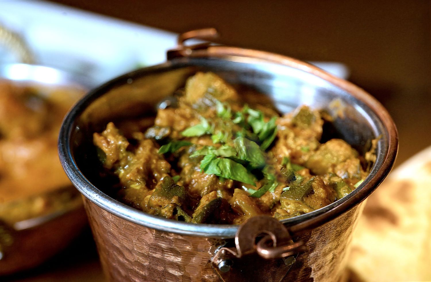 A rich Indian curry served in a traditional copper karahi pot, garnished with fresh cilantro leaves.