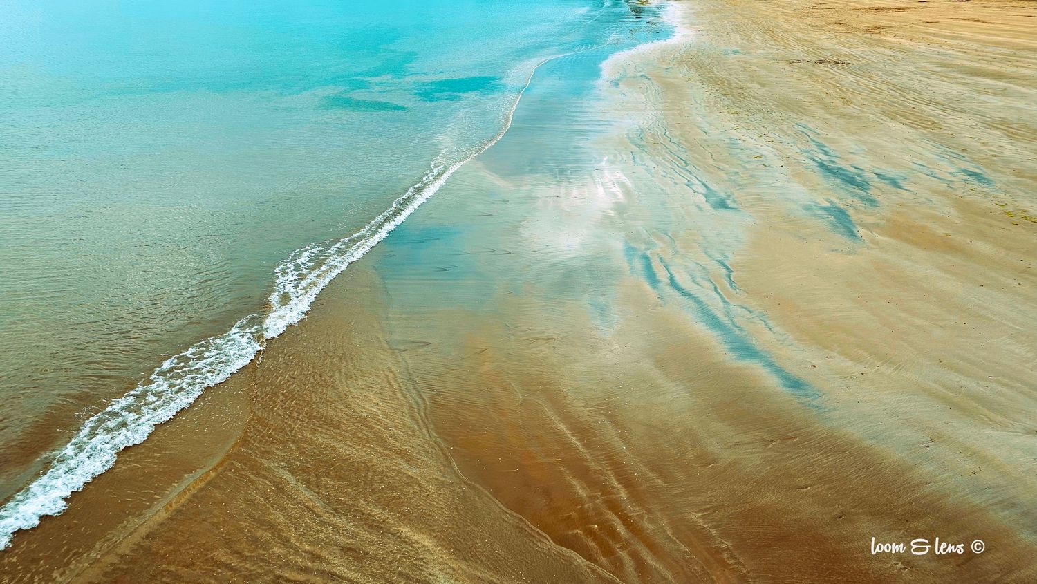 Aerial view of coastline where turquoise ocean meets sandy beach.