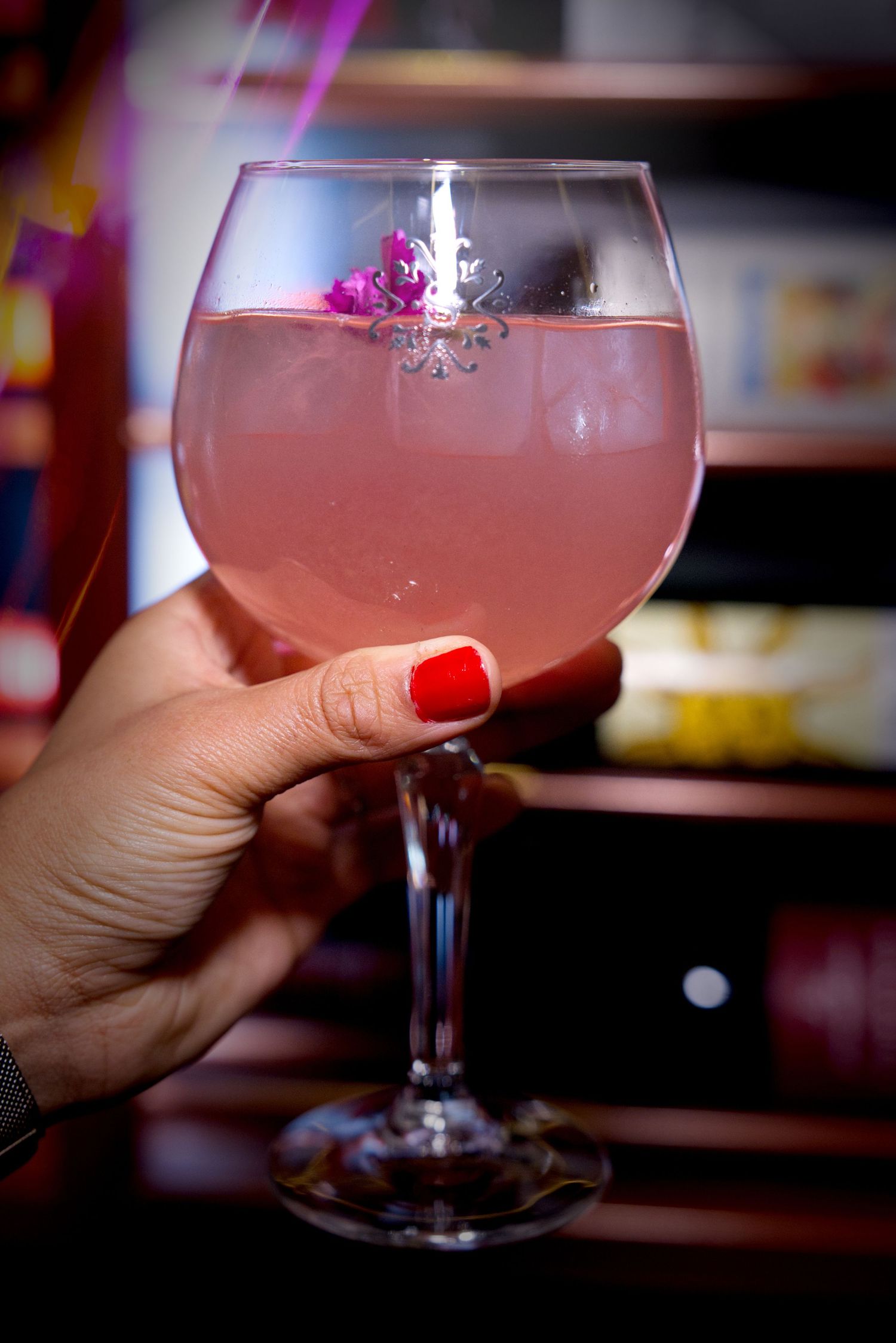 A hand holds a large snifter glass filled with a pink cocktail in a dimly lit setting.
