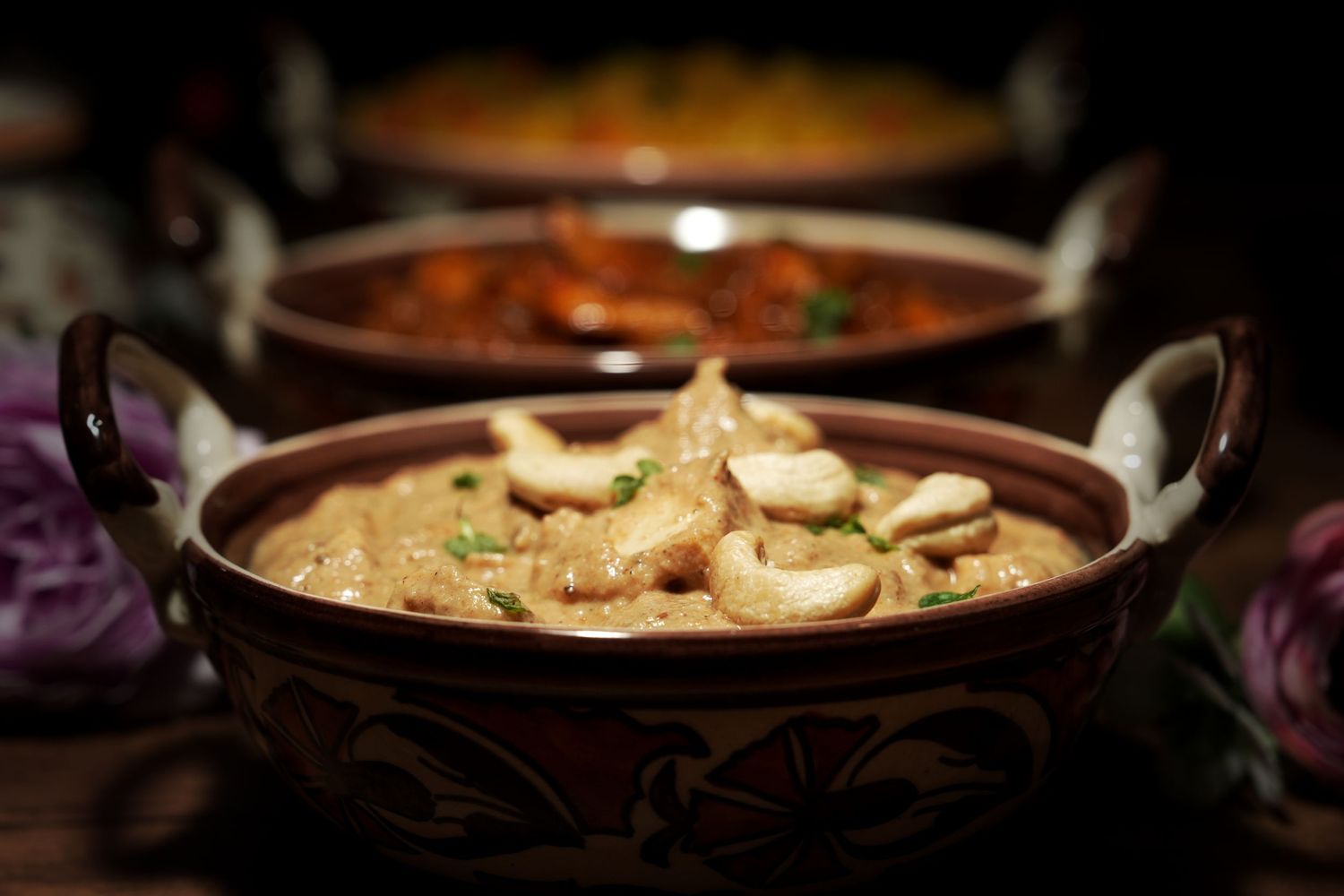 Steaming hot curry dish in a traditional clay pot with rich sauce and garnish.
