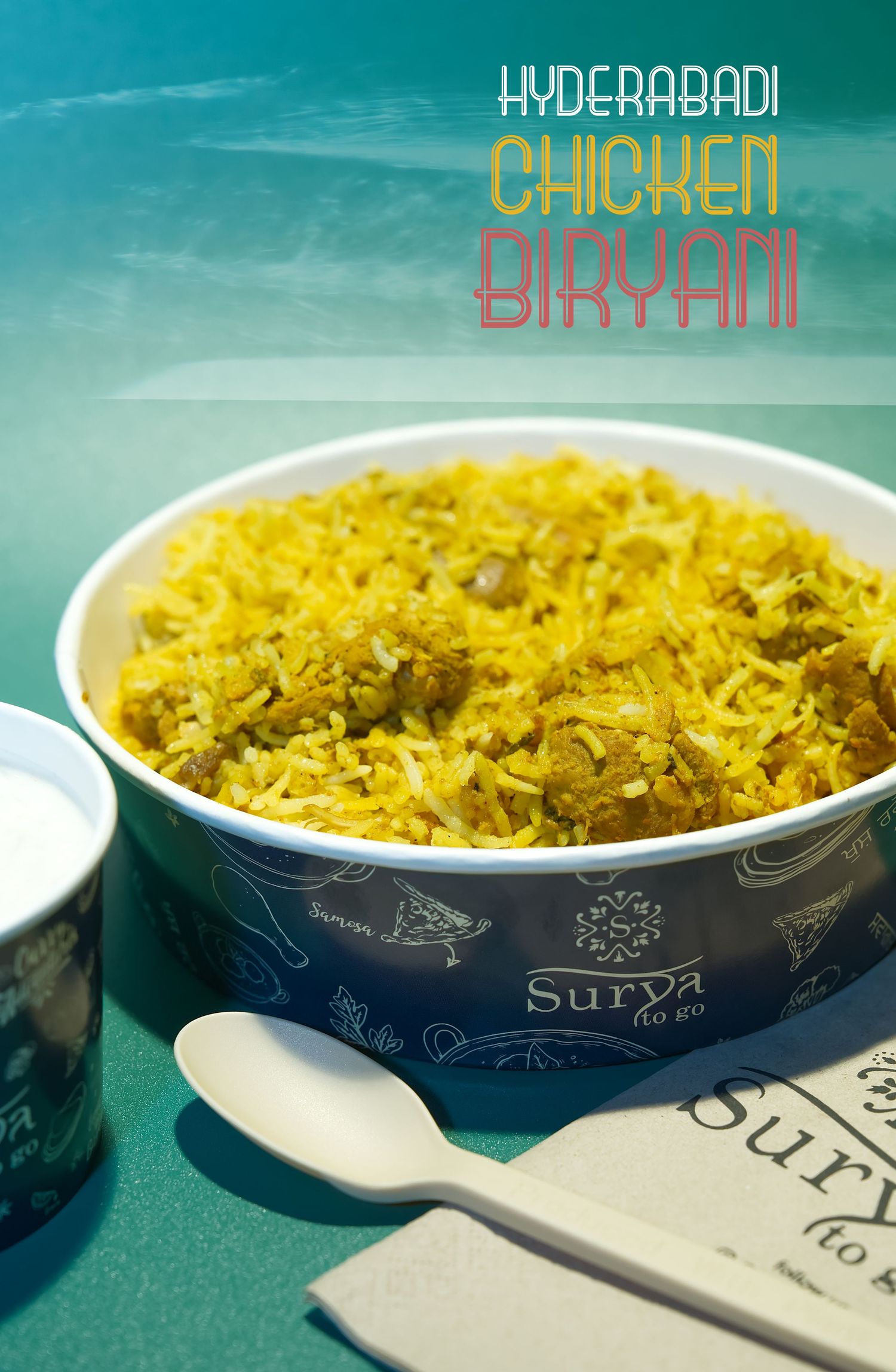 Steaming bowl of yellow Hyderabadi chicken biryani served in a decorative blue and white dish against turquoise background.