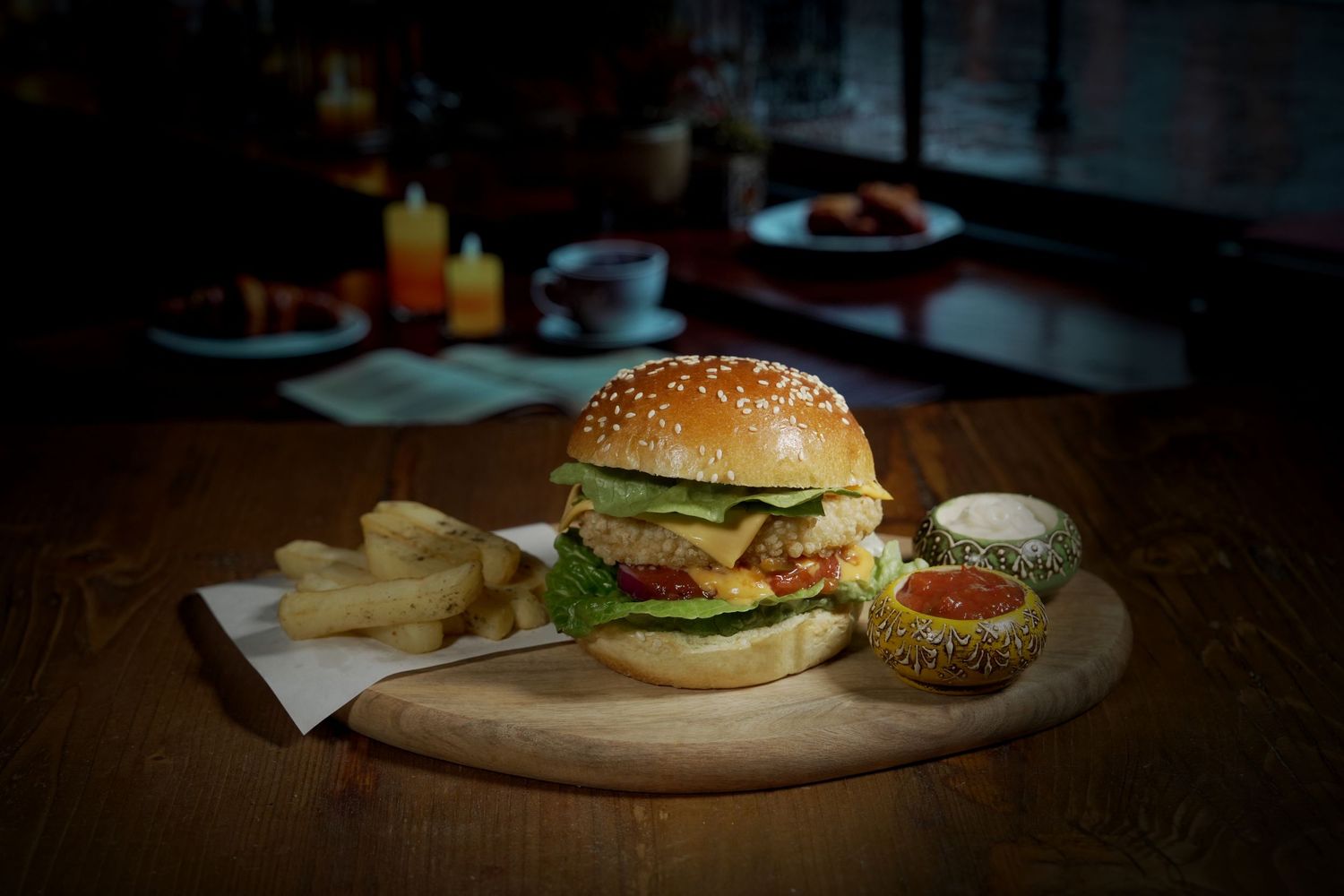 Gourmet burger with fries served on wooden board in moody restaurant lighting.