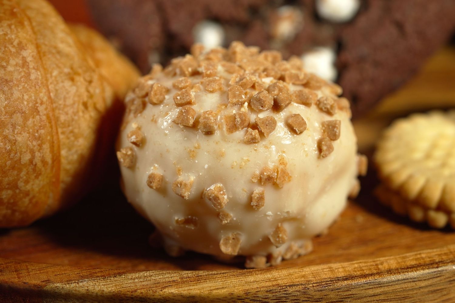 Close-up of glazed donuts with toffee crumbs on a rustic wooden board.