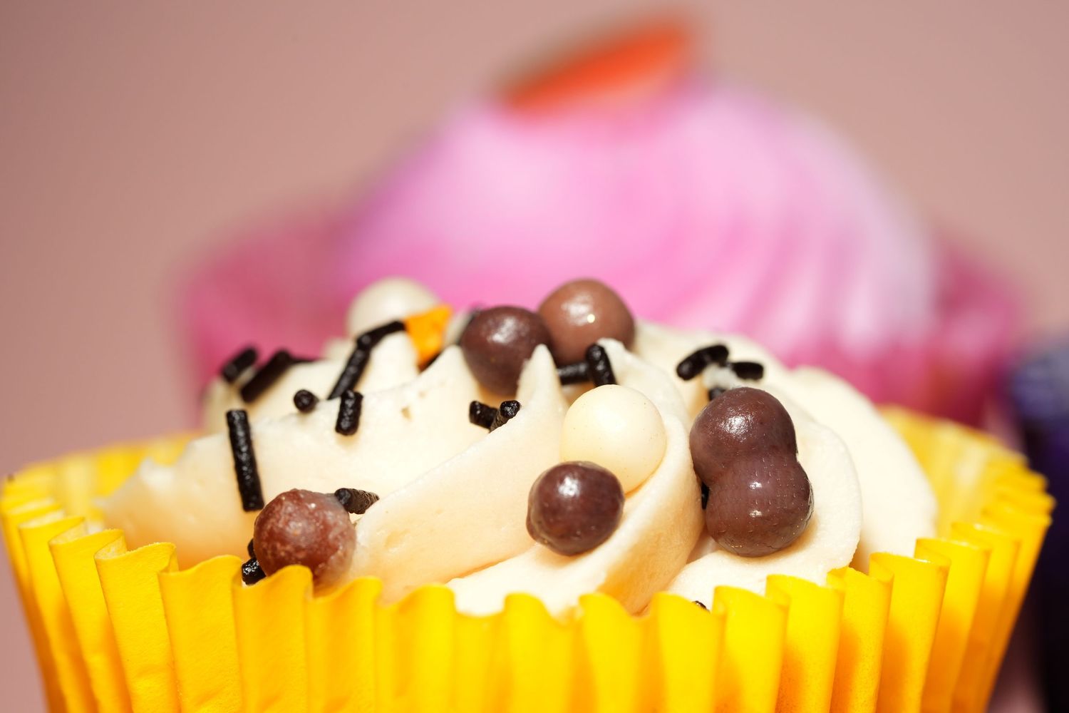 Cupcake topped with white frosting and chocolate chips in yellow wrapper.