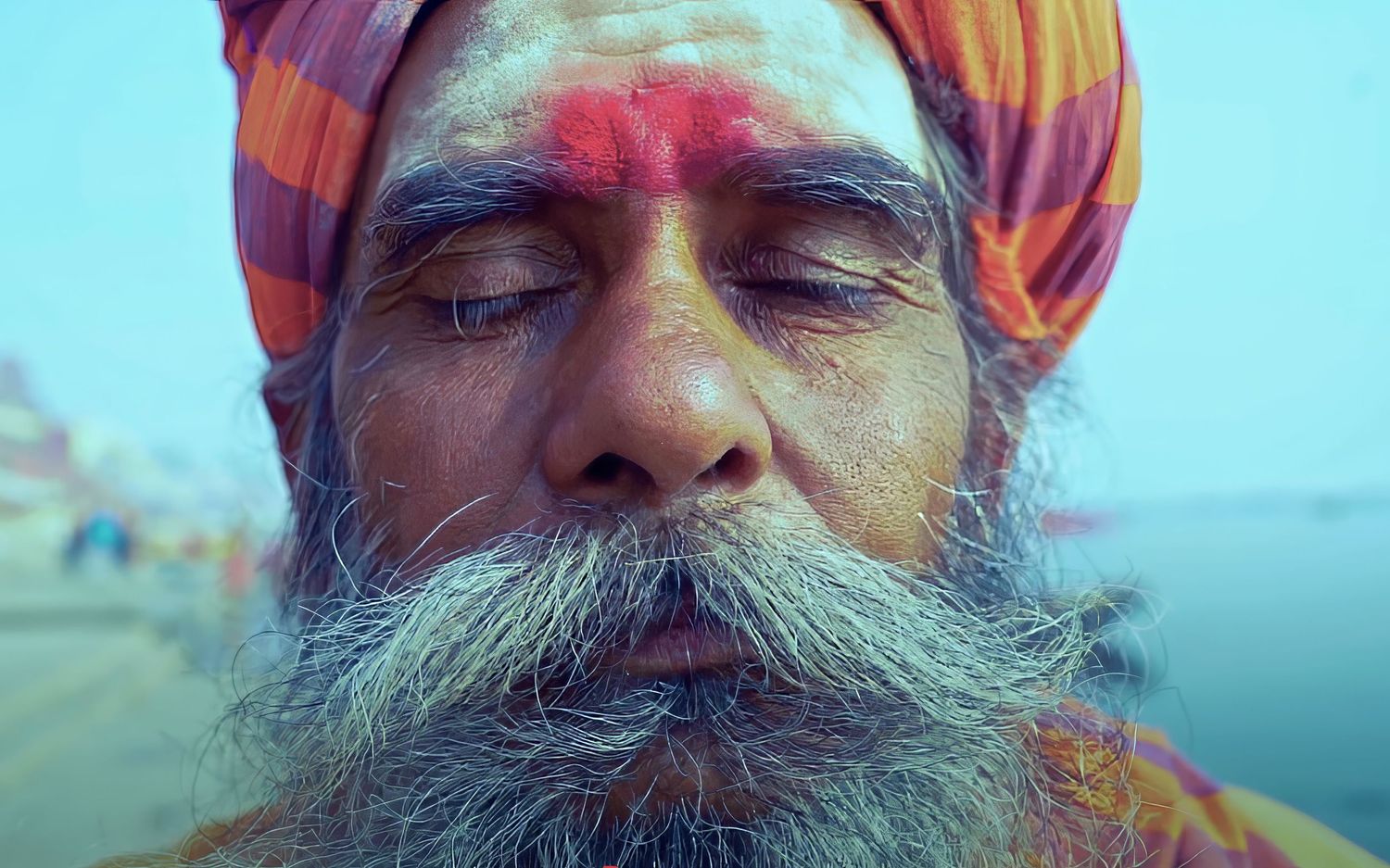 Portrait of a Sadhu holy man wearing orange turban with vibrant colors against blue sky.