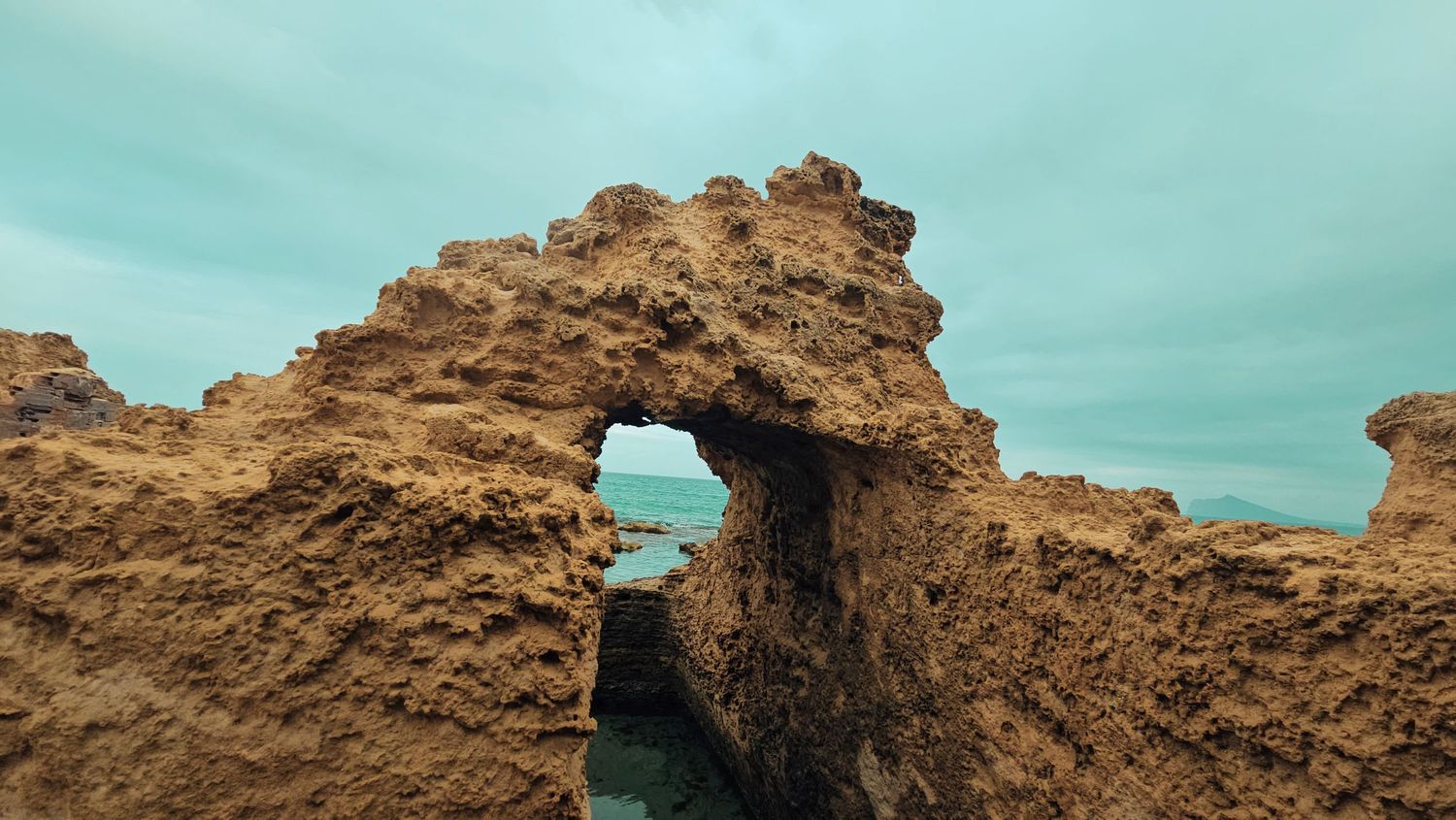 Natural rock arch formation against turquoise sky creating dramatic coastal landscape view.