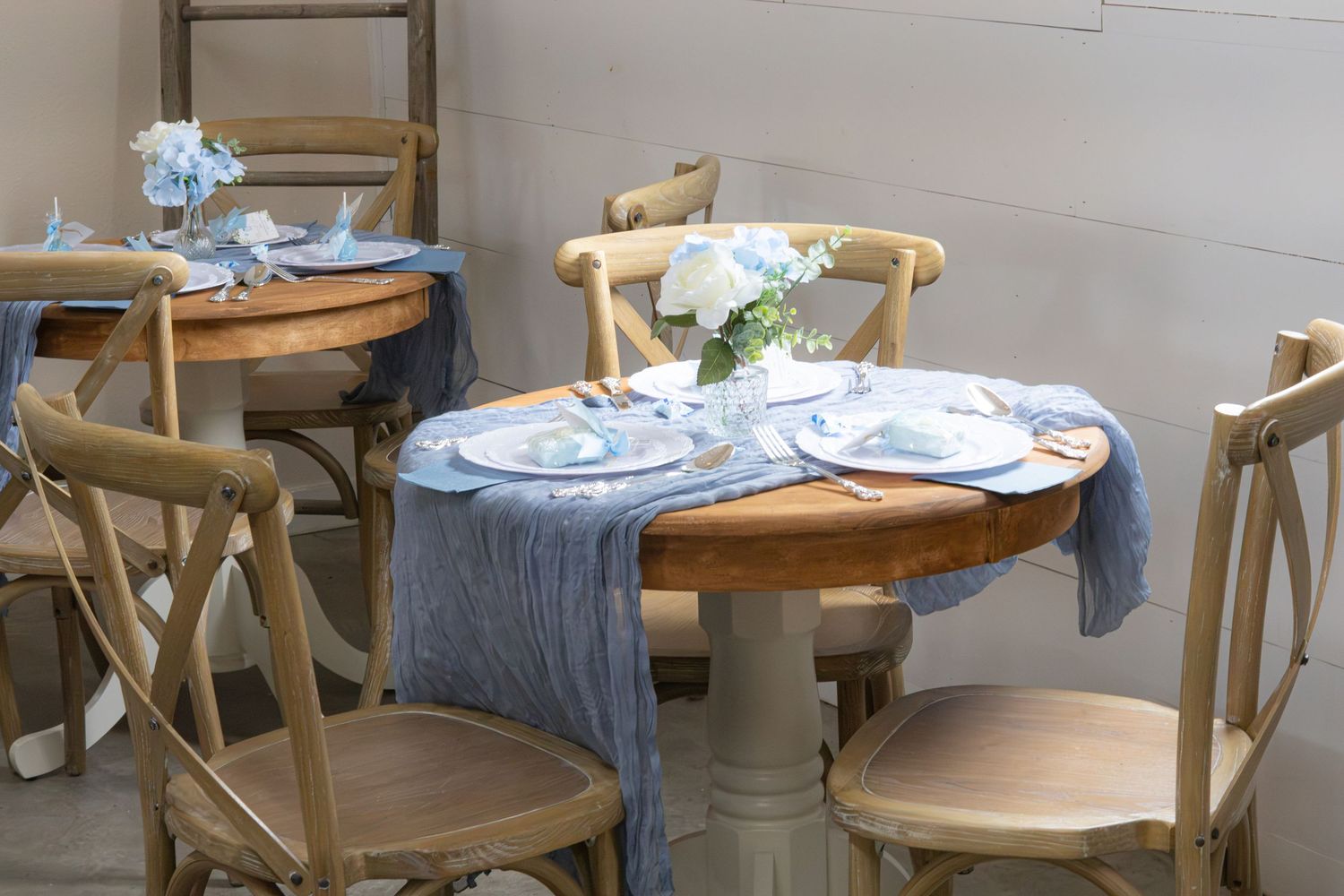 Round wooden table with cross-back chairs, blue hydrangea centerpiece and gray runner set for a baby shower celebration.