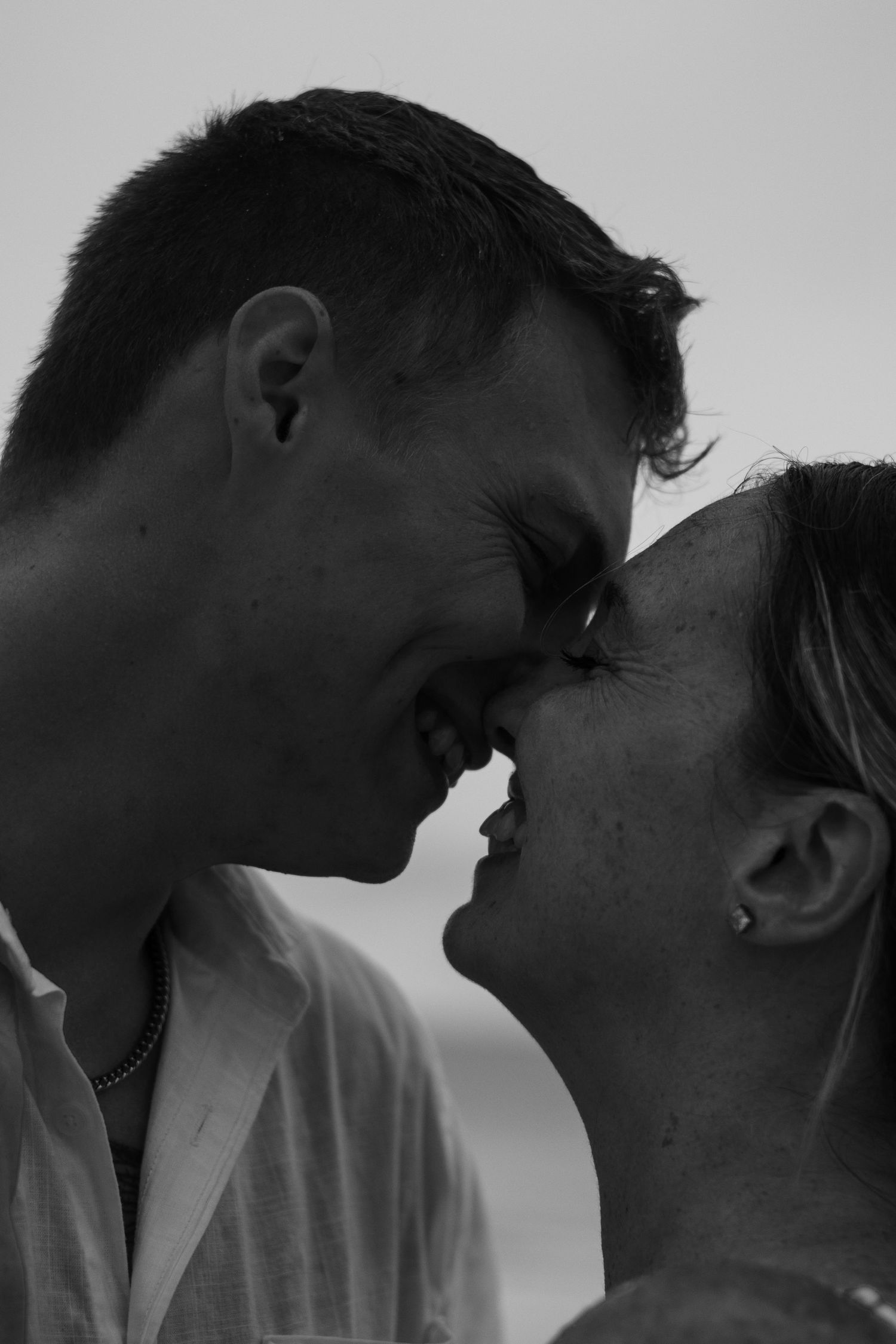 Black and white close-up of a smiling couple touching foreheads and noses in an intimate, joyful moment.